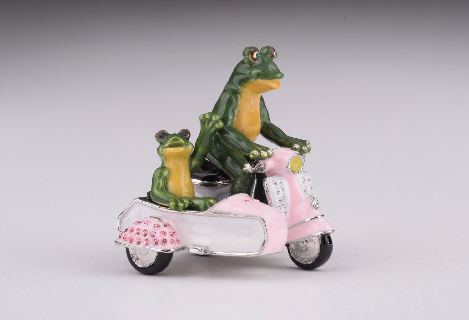 A whimsical trinket box featuring frogs riding a Vespa with a sidecar, adorned with Austrian crystals and gold plating.