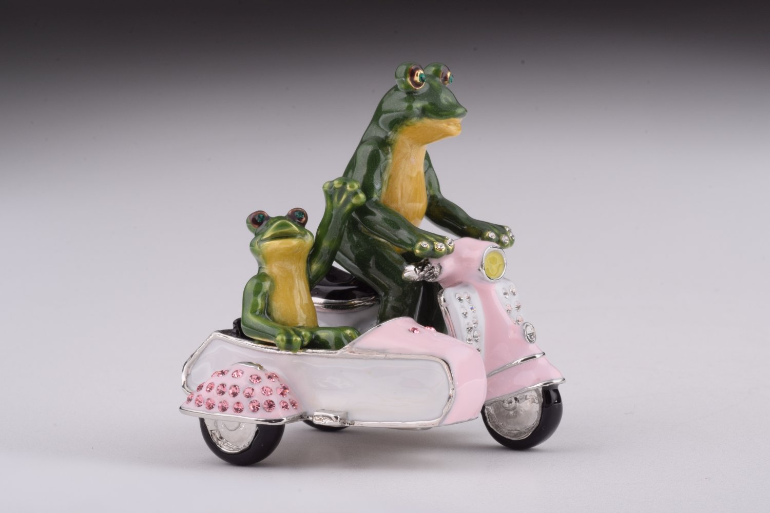 A whimsical trinket box featuring frogs riding a Vespa with a sidecar, adorned with Austrian crystals and gold plating.