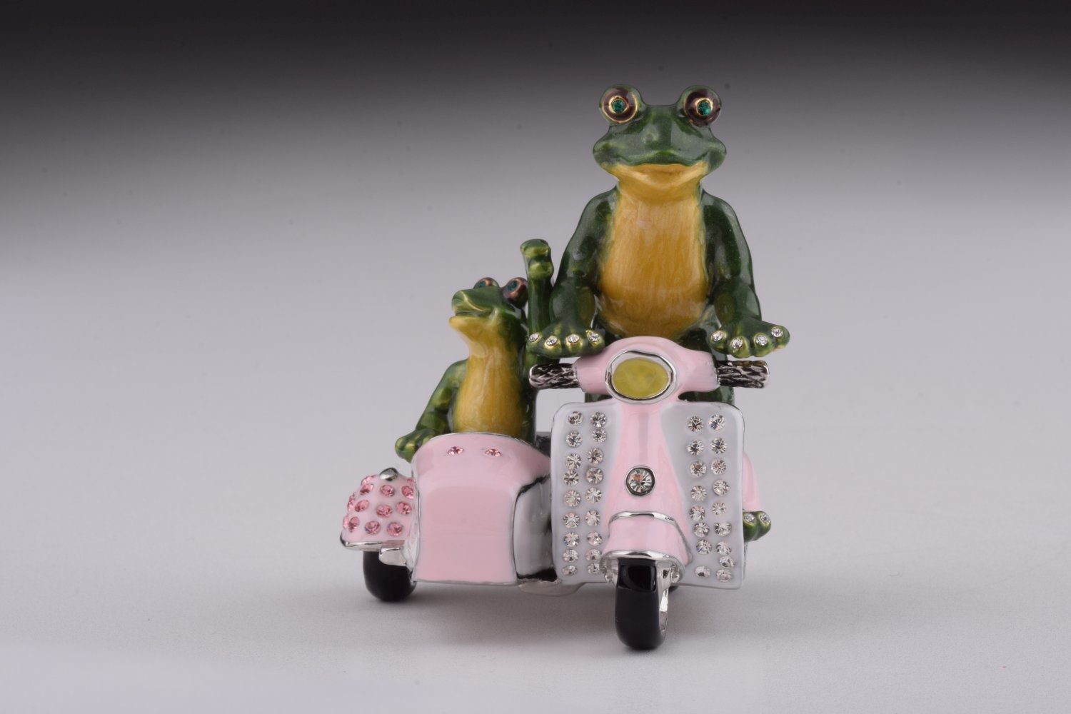 A whimsical trinket box featuring frogs riding a Vespa with a sidecar, adorned with Austrian crystals and gold plating.