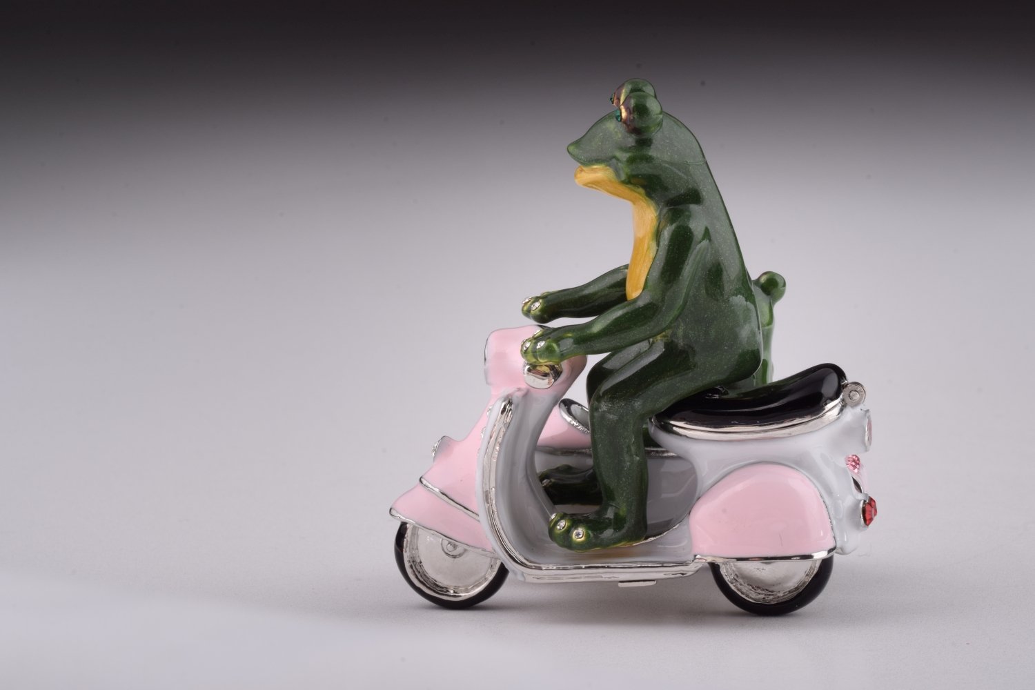 A whimsical trinket box featuring frogs riding a Vespa with a sidecar, adorned with Austrian crystals and gold plating.