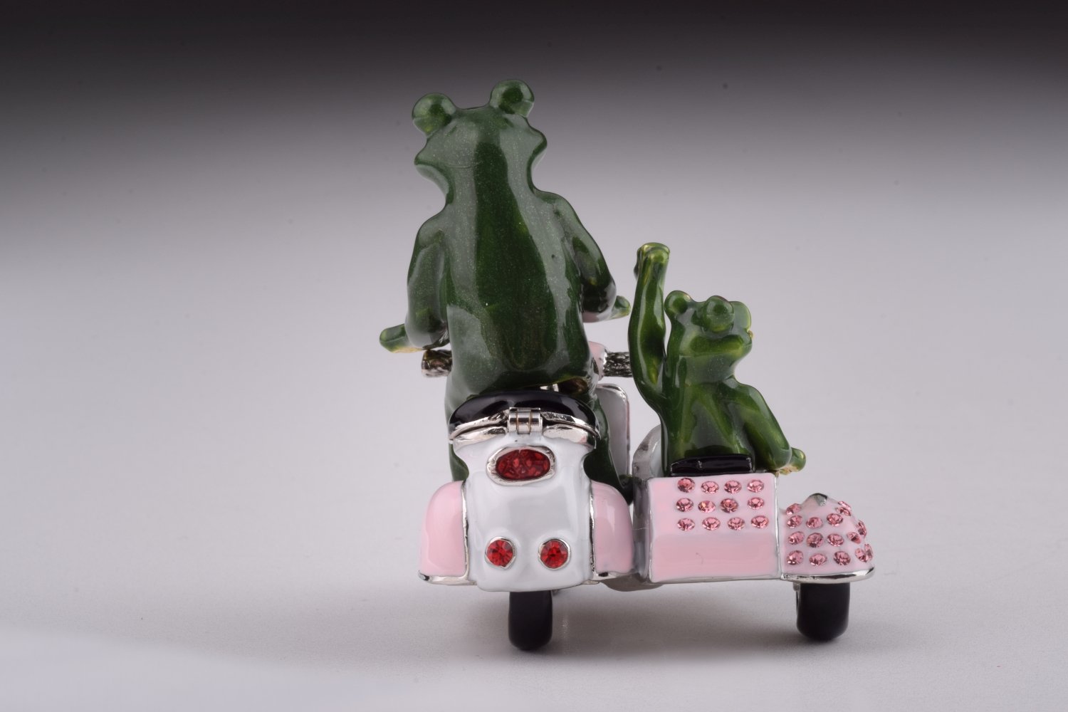 A whimsical trinket box featuring frogs riding a Vespa with a sidecar, adorned with Austrian crystals and gold plating.