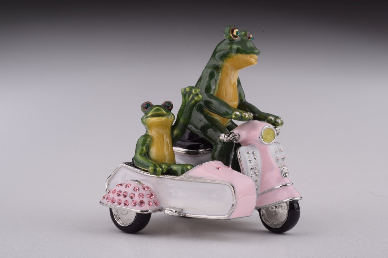 A whimsical trinket box featuring frogs riding a Vespa with a sidecar, adorned with Austrian crystals and gold plating.