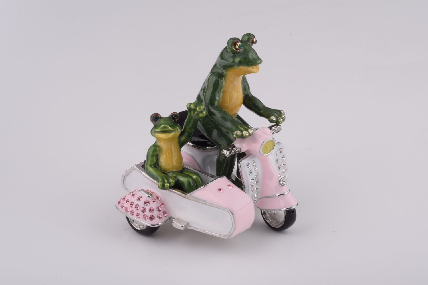 A whimsical trinket box featuring frogs riding a Vespa with a sidecar, adorned with Austrian crystals and gold plating.