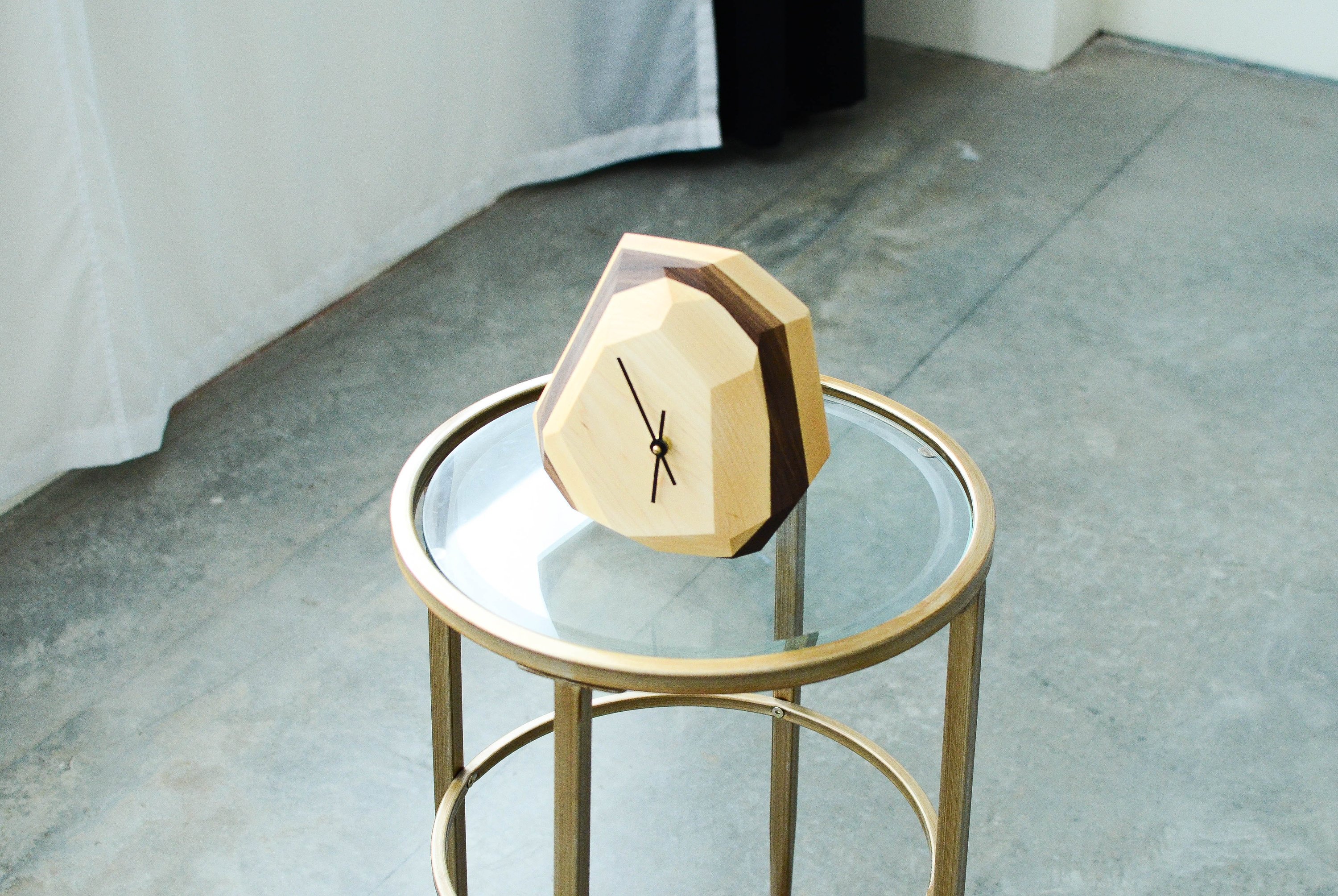 A modern geometric wall and table clock made from American hardwood, showcasing unique wood grain patterns and a quartz crystal-inspired design.