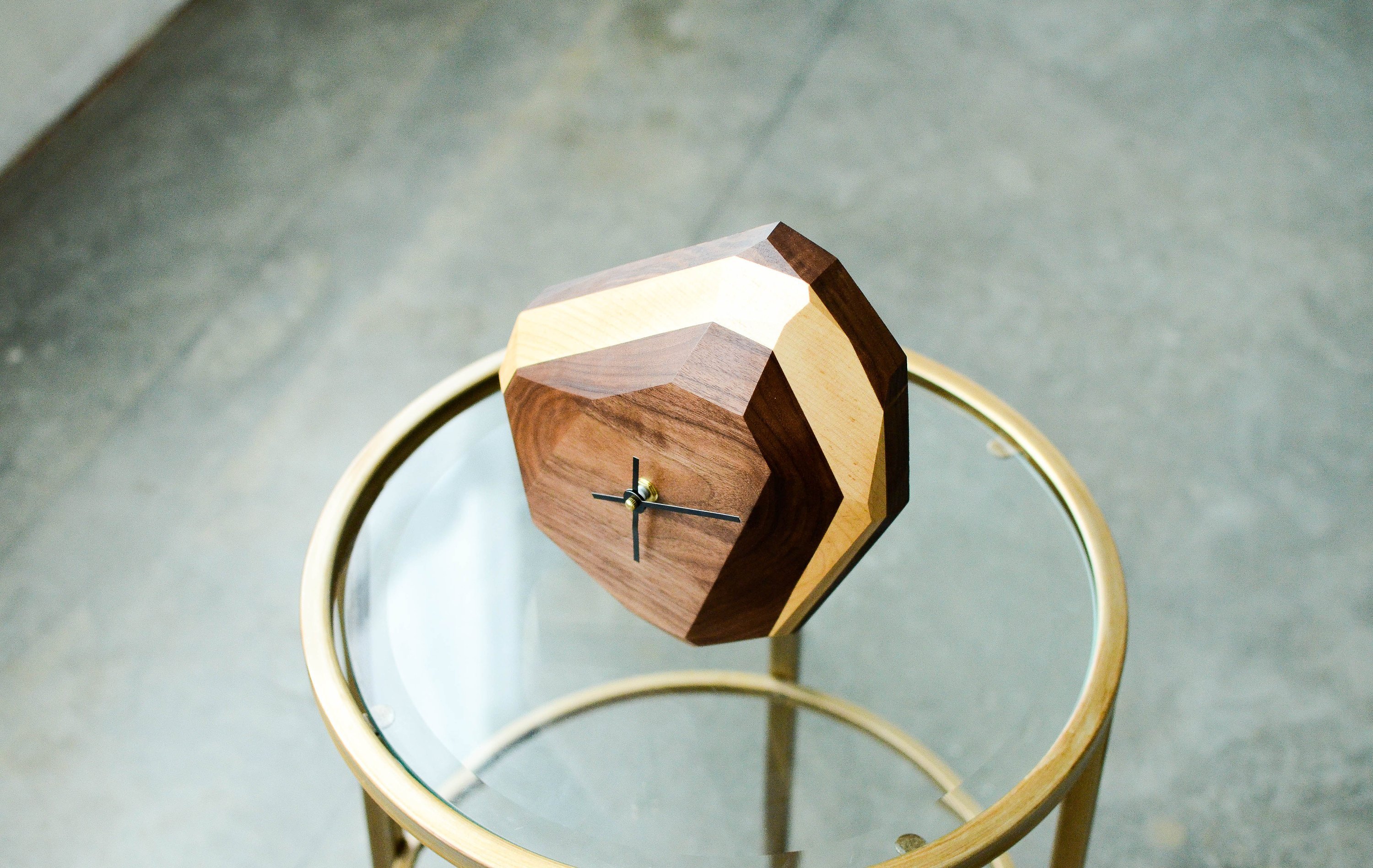 A modern geometric wall and table clock made from American hardwood, showcasing unique wood grain patterns and a quartz crystal-inspired design.