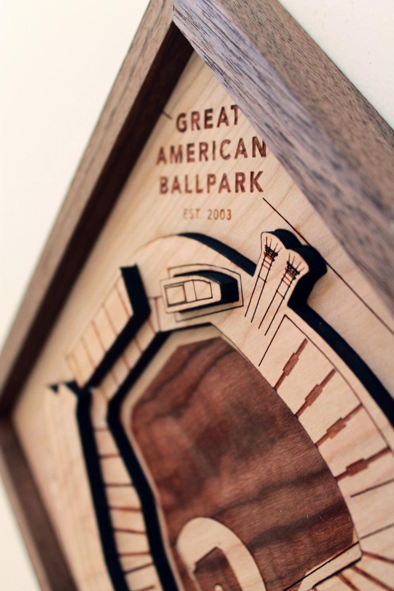 A beautifully crafted wooden model of the Great American Ballpark, featuring intricate details like smokestacks and a riverboat, framed in black walnut.