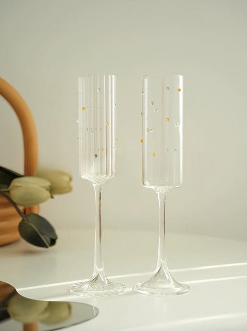 A set of two handblown champagne flutes featuring vibrant rainbow sprinkles, showcasing their whimsical design and high-quality crystal glass.