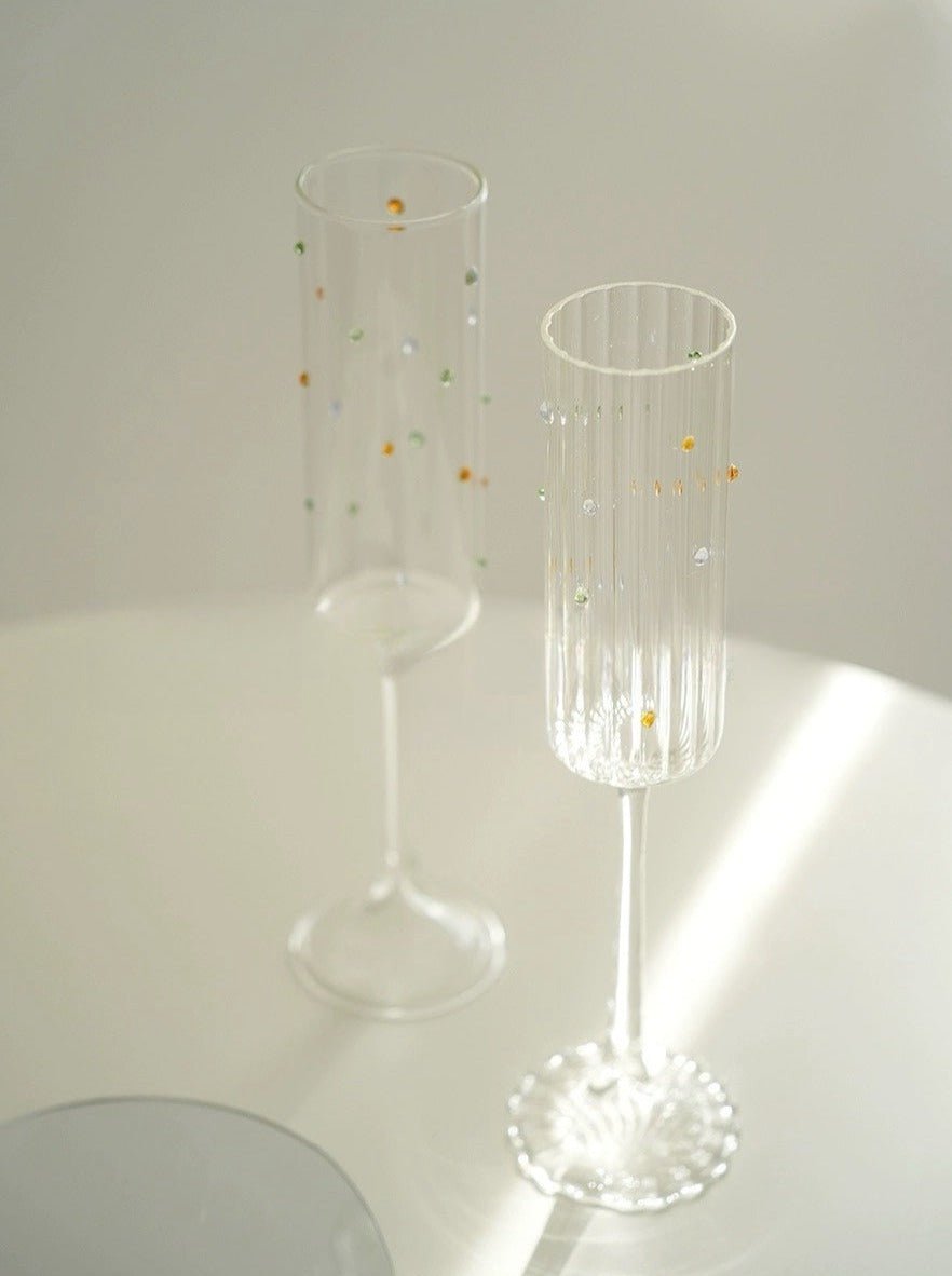 A set of two handblown champagne flutes featuring vibrant rainbow sprinkles, showcasing their whimsical design and high-quality crystal glass.