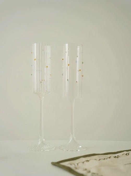 A set of two handblown champagne flutes featuring vibrant rainbow sprinkles, showcasing their whimsical design and high-quality crystal glass.