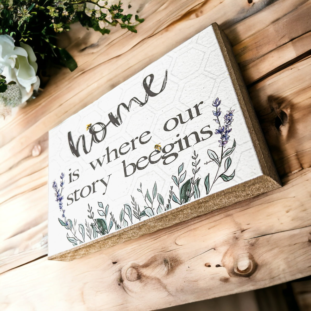 A decorative wooden block sign that reads 'HOME IS WHERE OUR STORY BEEGINS', featuring a rustic design suitable for various home decor styles.