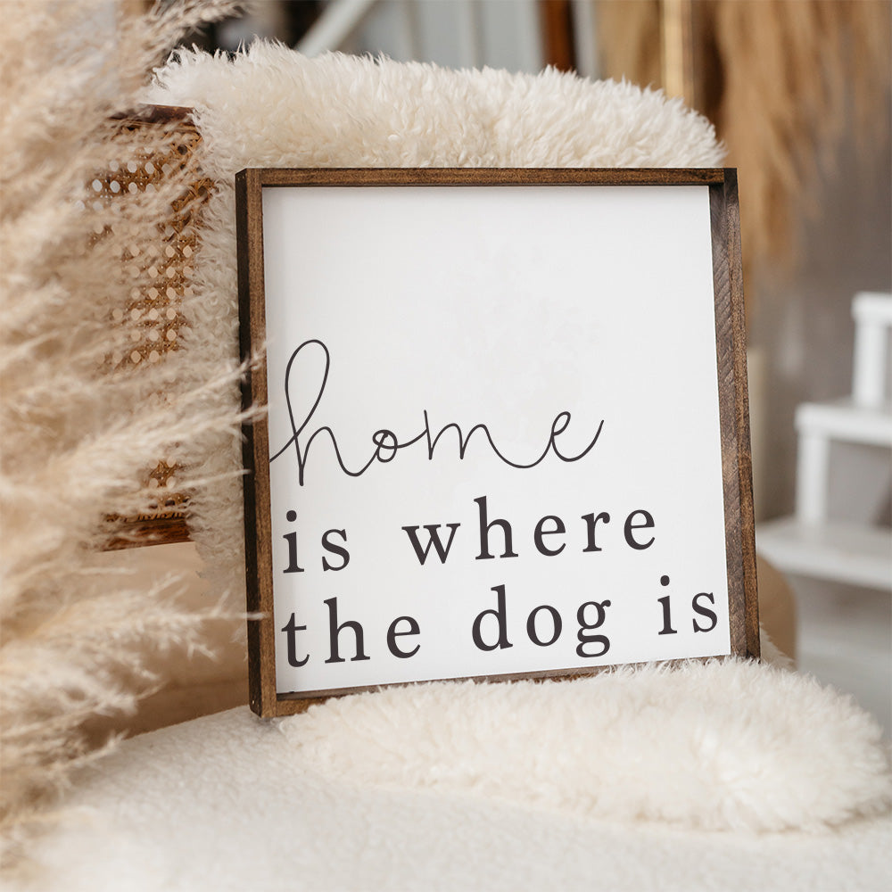 A rustic wood sign that reads 'Home Is Where The Dog Is', featuring a pine wood frame and a white background.