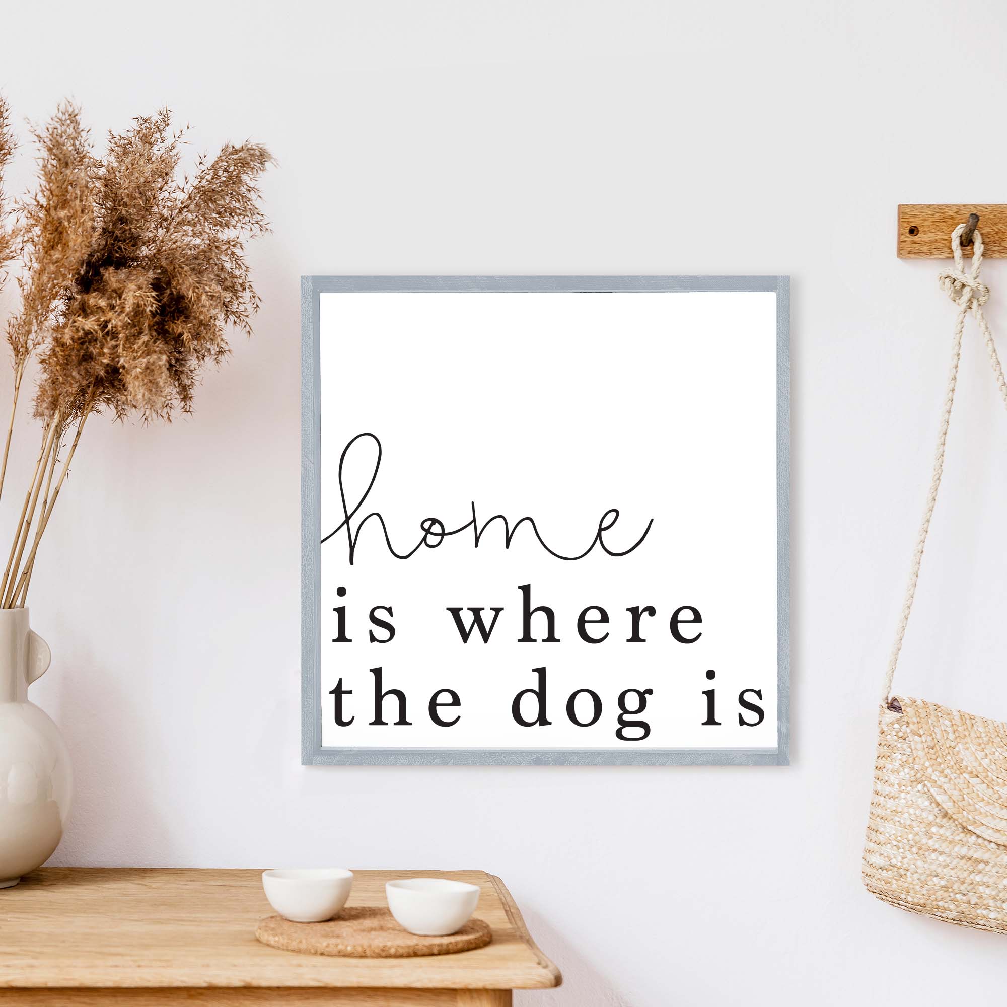 A rustic wood sign that reads 'Home Is Where The Dog Is', featuring a pine wood frame and a white background.