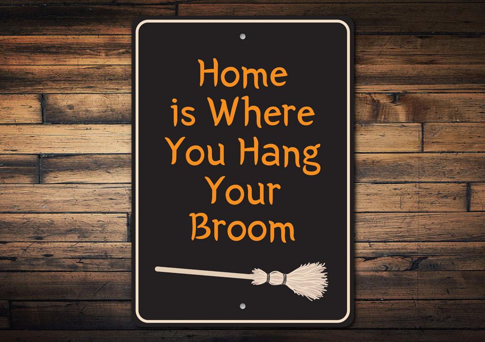 A decorative metal sign reading 'Home is Where You Hang Your Broom', featuring spooky Halloween-themed design elements.