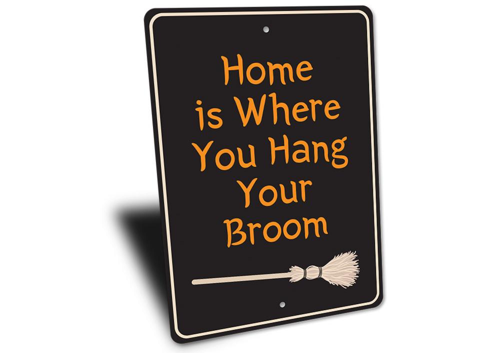 A decorative metal sign reading 'Home is Where You Hang Your Broom', featuring spooky Halloween-themed design elements.