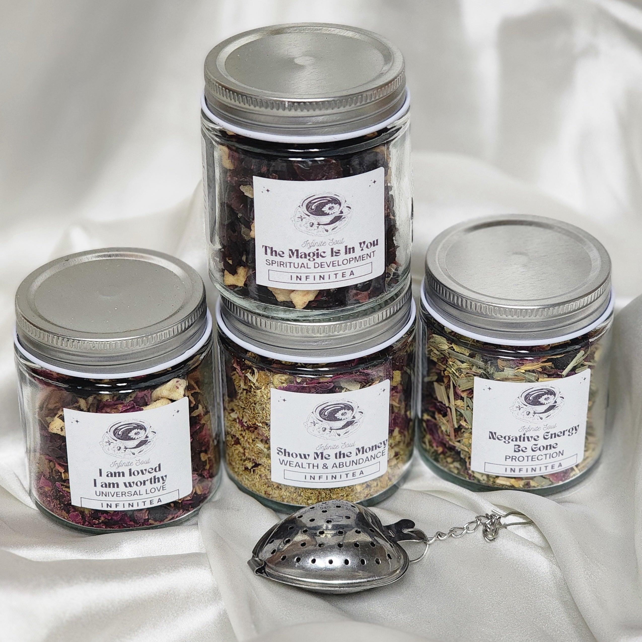 Infinitea Spellbound Bundle Pack featuring four herbal tea blends and a strawberry tea infuser, beautifully arranged.