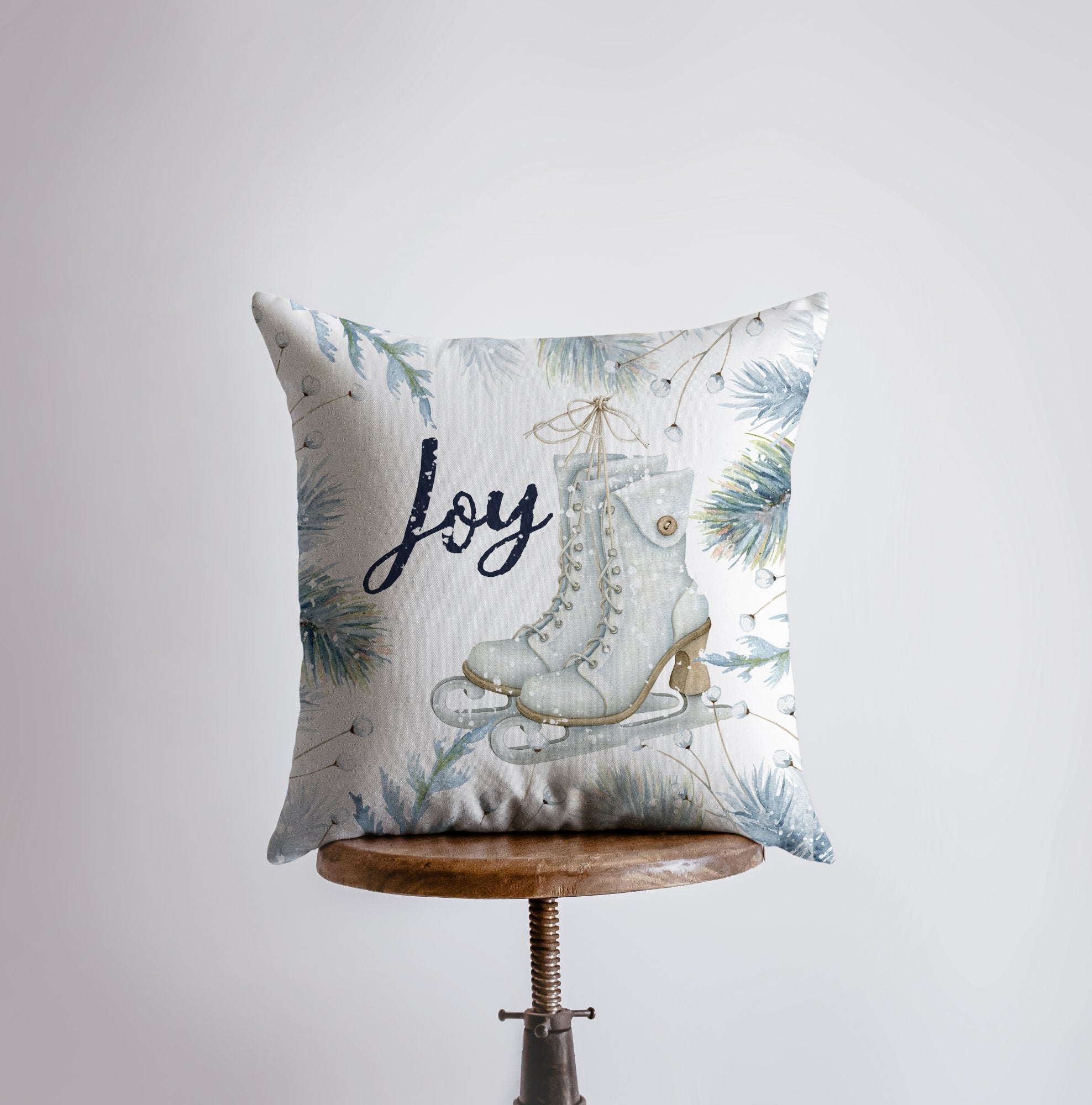 Joy Ice Skating Throw Pillow featuring white ice skates and cursive 'Joy' text with wintergreen branches, perfect for winter decor.