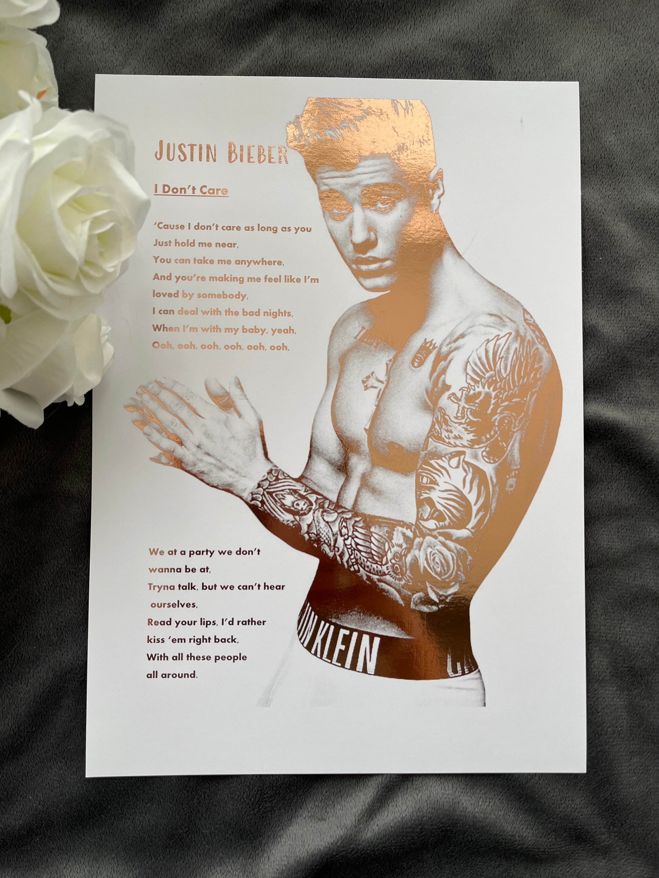 A stunning foil print of Justin Bieber featuring a rose gold portrait and song lyrics on a white background.