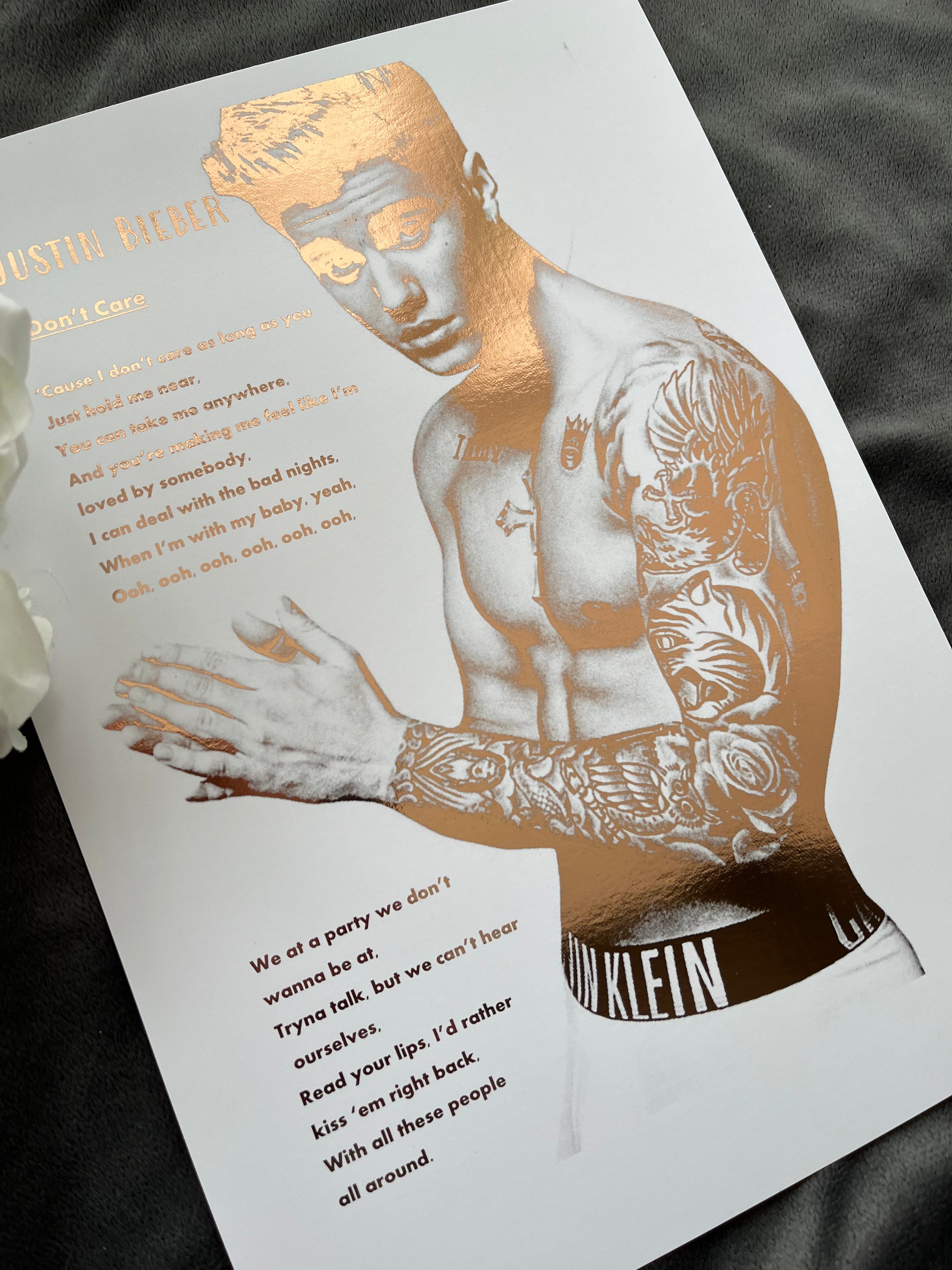 A stunning foil print of Justin Bieber featuring a rose gold portrait and song lyrics on a white background.