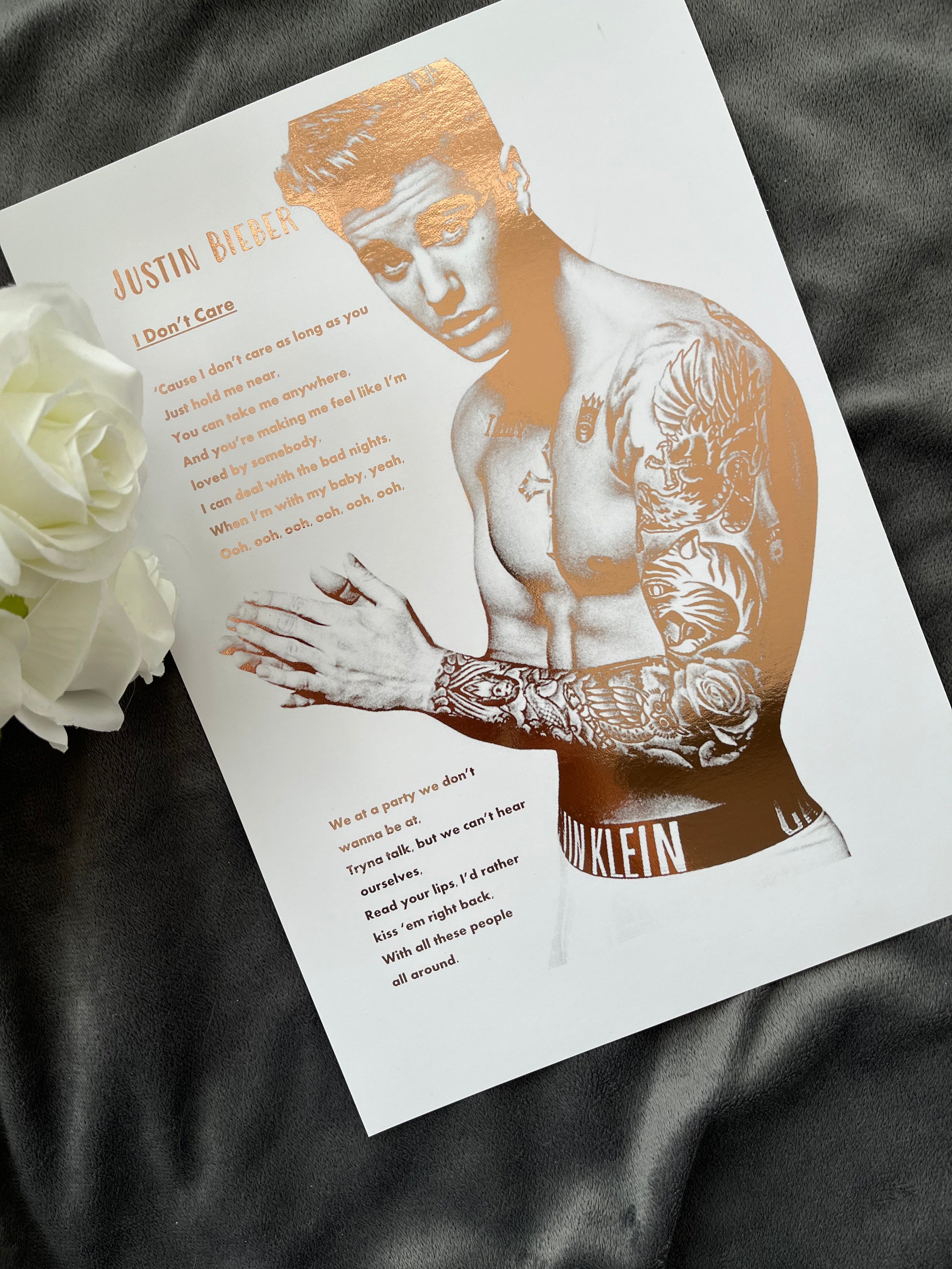 A stunning foil print of Justin Bieber featuring a rose gold portrait and song lyrics on a white background.