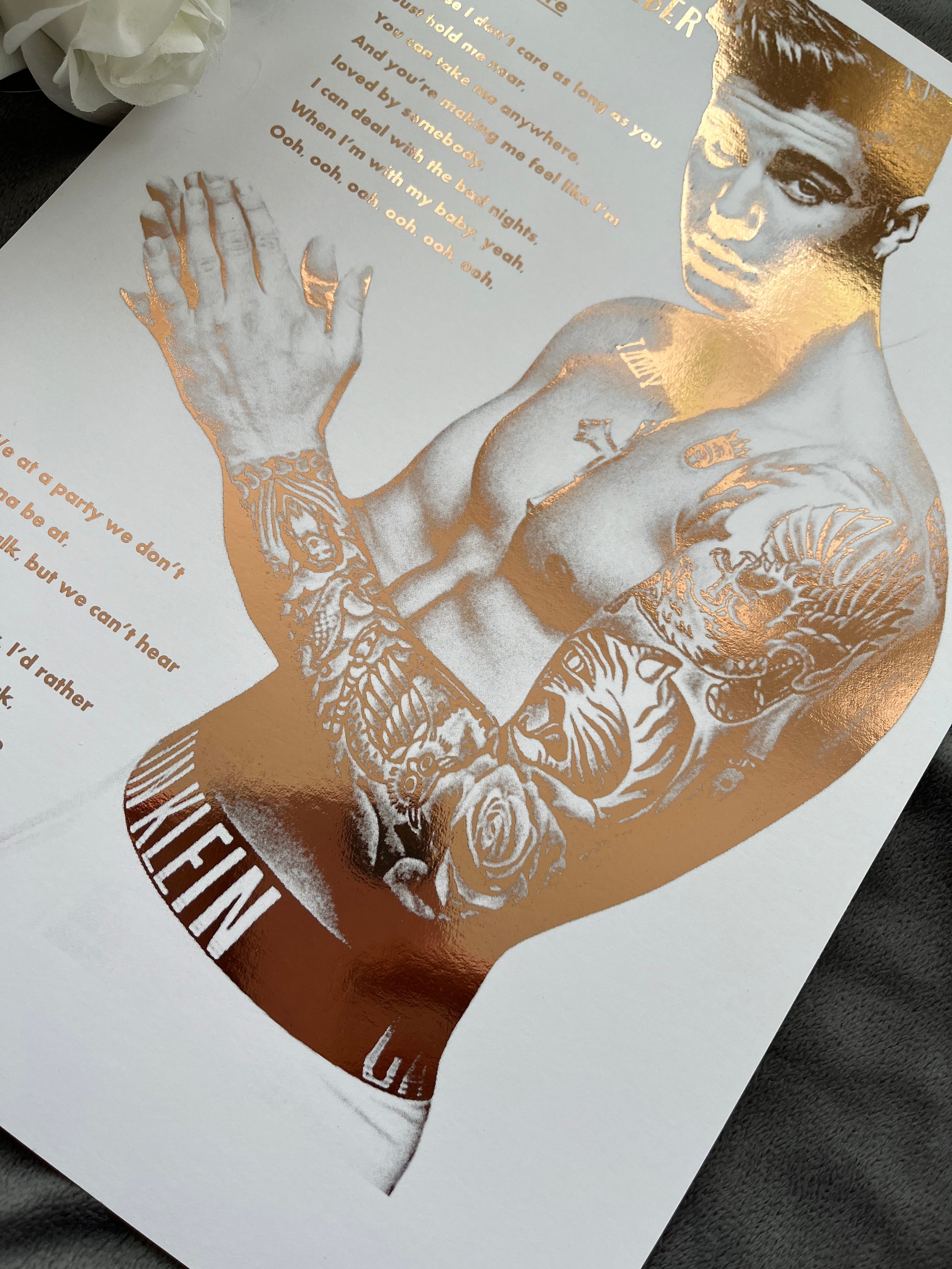 A stunning foil print of Justin Bieber featuring a rose gold portrait and song lyrics on a white background.