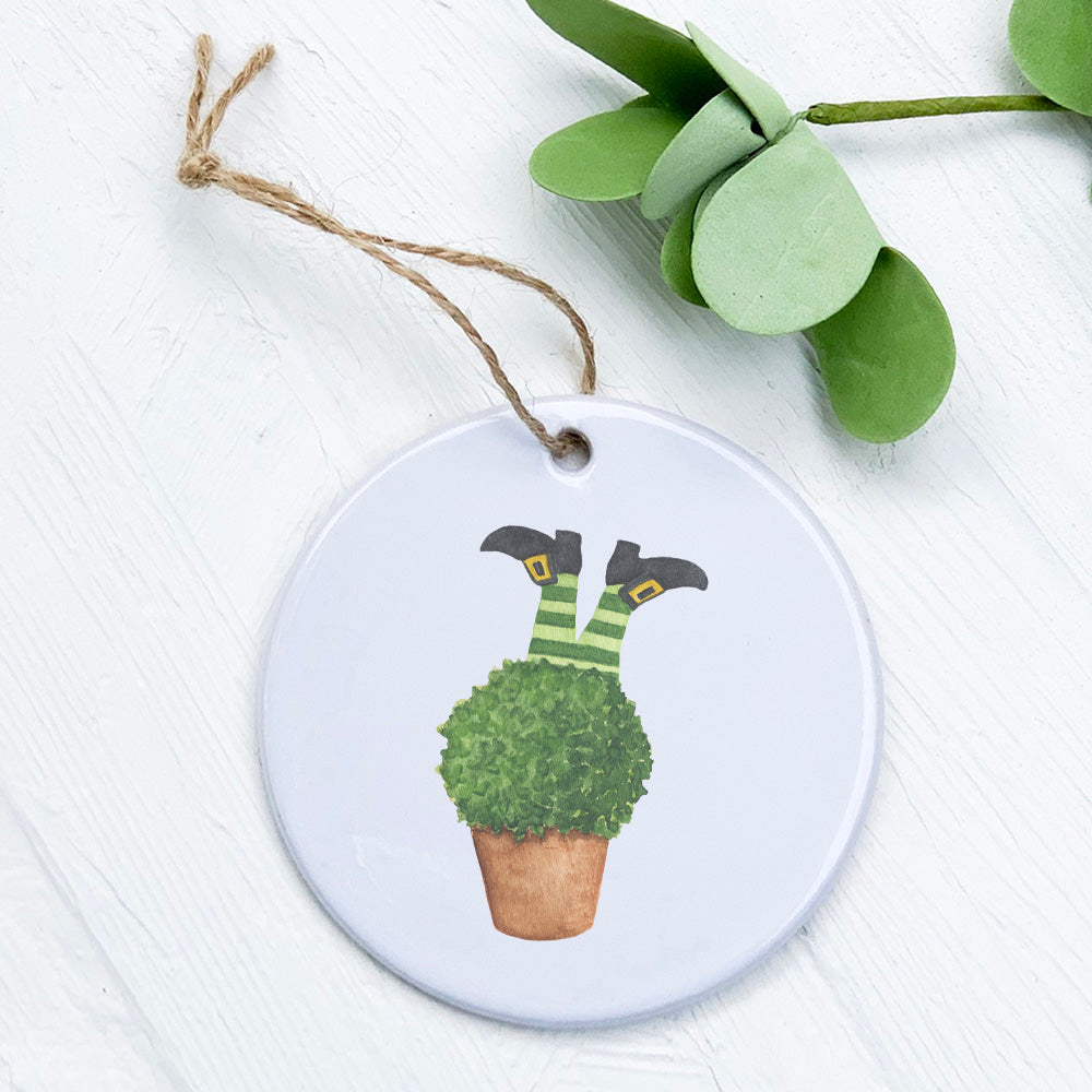 A whimsical porcelain ornament featuring leprechaun legs nestled in a plant, showcasing vibrant colors and intricate details.