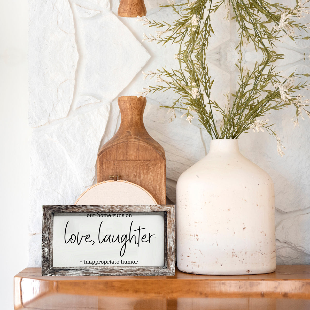 A vintage-style wooden sign that reads 'Our Home Runs on Love, Laughter + Inappropriate Humor', made from durable Paulownia wood.