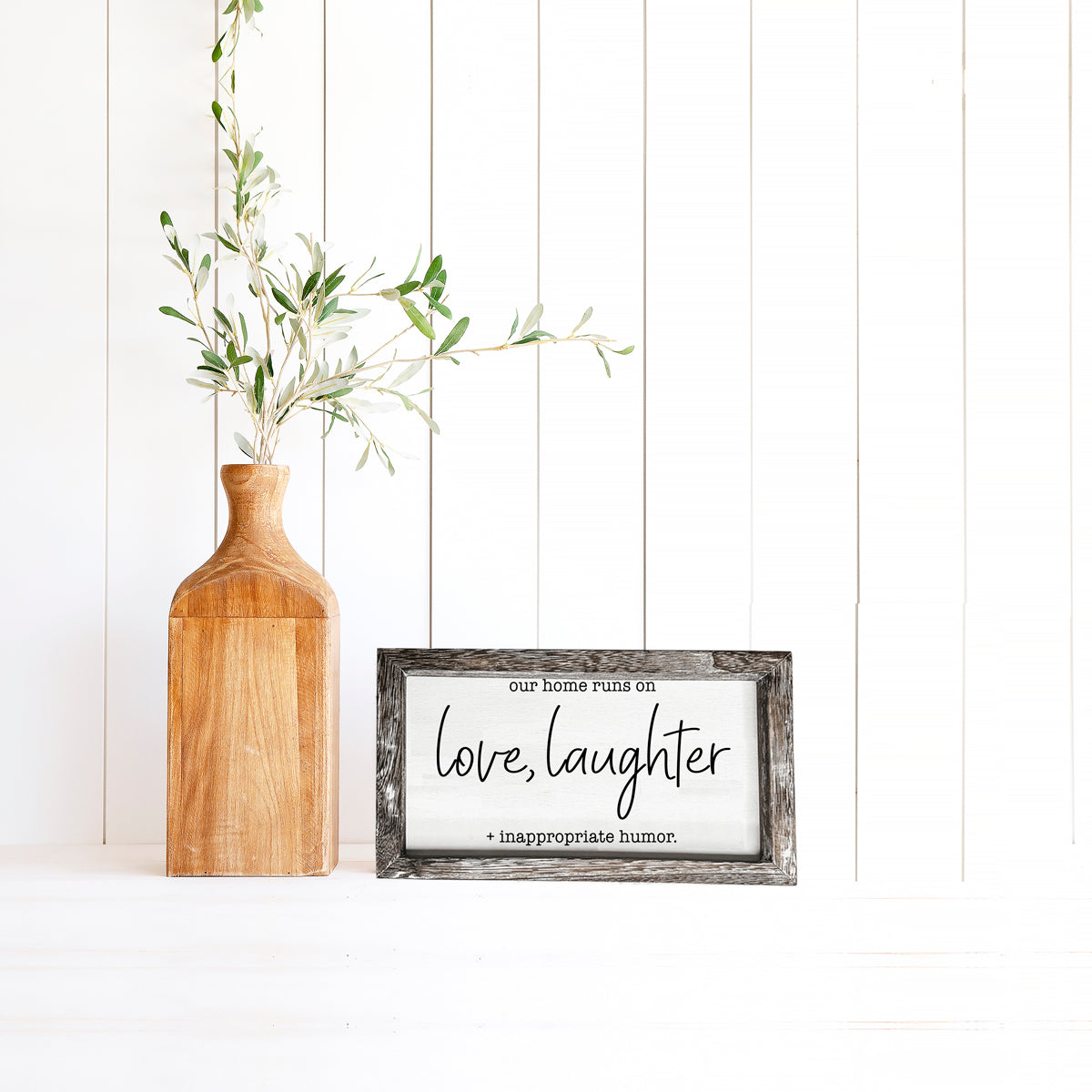 A vintage-style wooden sign that reads 'Our Home Runs on Love, Laughter + Inappropriate Humor', made from durable Paulownia wood.