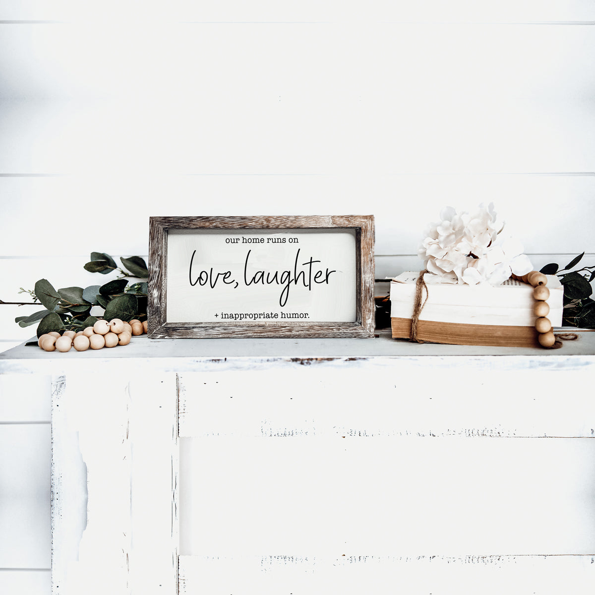 A vintage-style wooden sign that reads 'Our Home Runs on Love, Laughter + Inappropriate Humor', made from durable Paulownia wood.