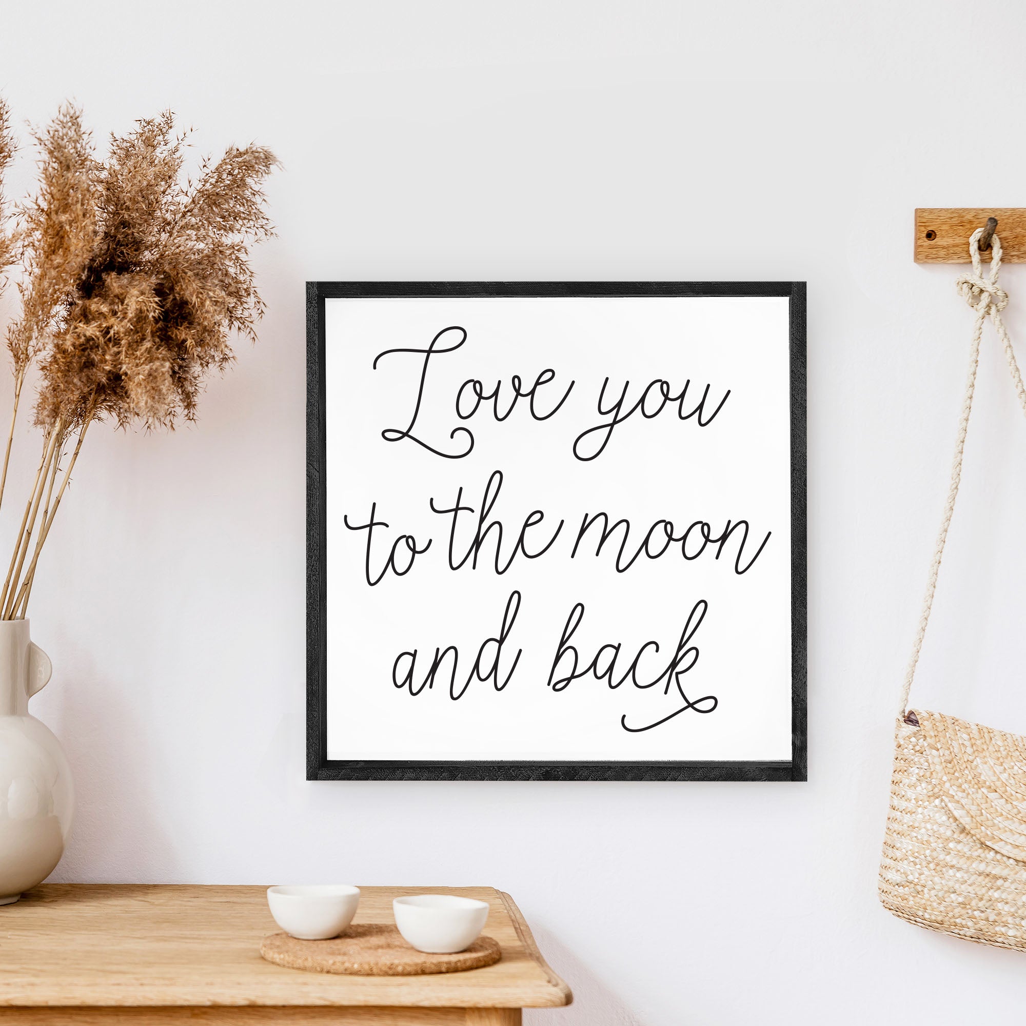 A rustic wood sign featuring the phrase 'Love You To The Moon And Back' in black text on a white background, framed in stained pine wood.