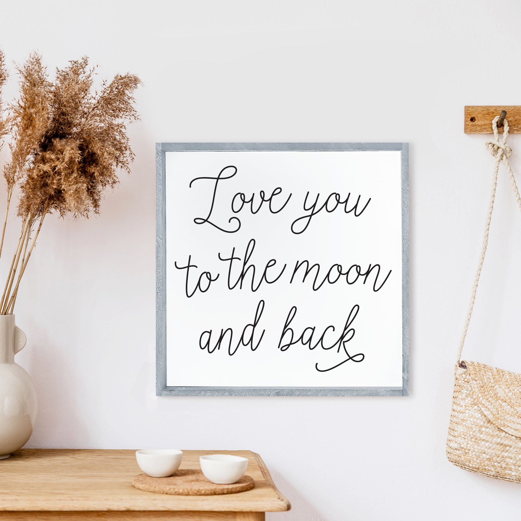 A rustic wood sign featuring the phrase 'Love You To The Moon And Back' in black text on a white background, framed in stained pine wood.