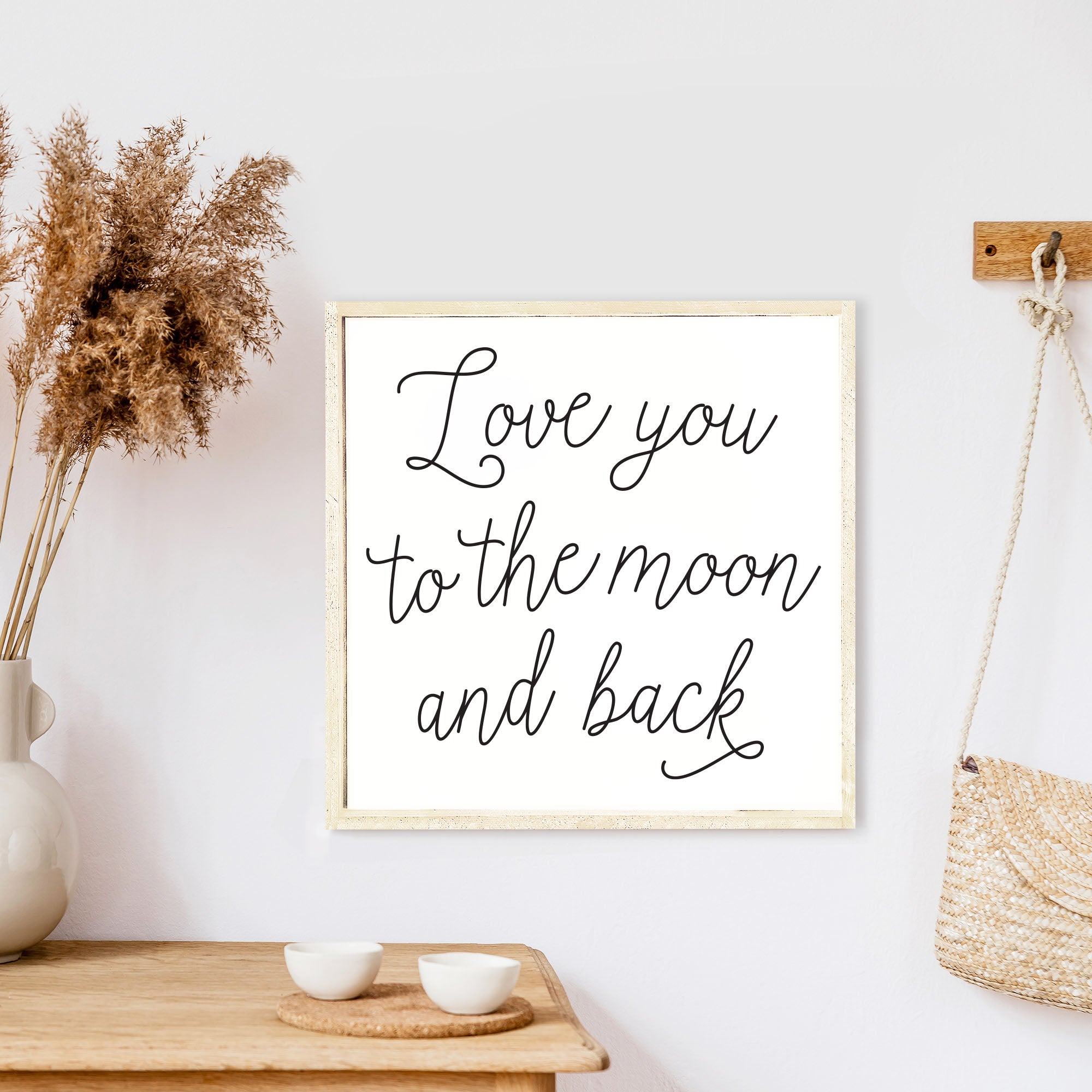 A rustic wood sign featuring the phrase 'Love You To The Moon And Back' in black text on a white background, framed in stained pine wood.