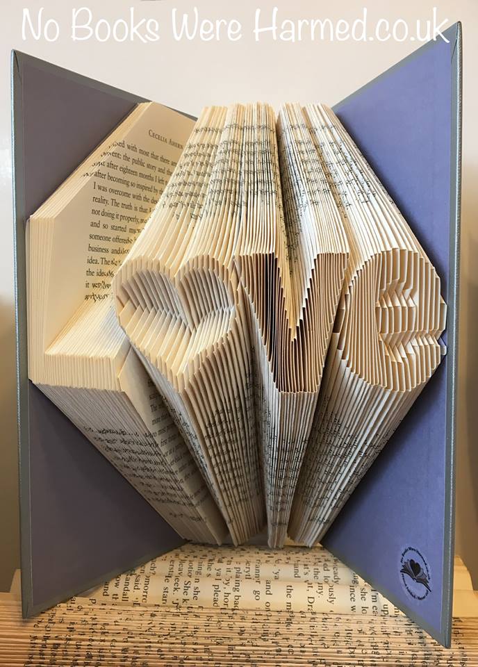 Unique hand-folded book art piece titled L♥ve, crafted from vintage books with intricate folds and varying colors.