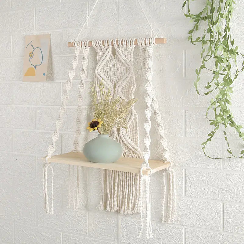 A beautifully handcrafted Macrame Wall Tapestry Plant Holder made from cotton cords, featuring a natural wooden shelf for plants or books.