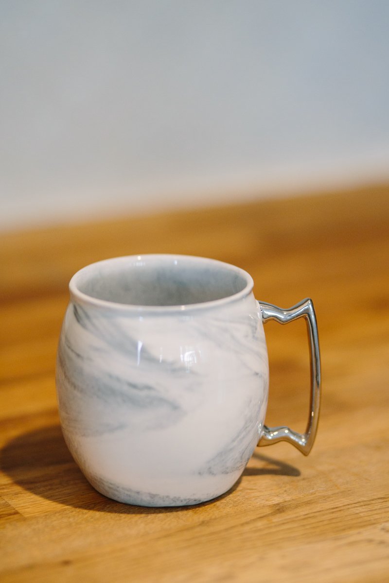 A stylish marble and silver coffee mug with a white interior, designed to resemble a Moscow Mule mug.