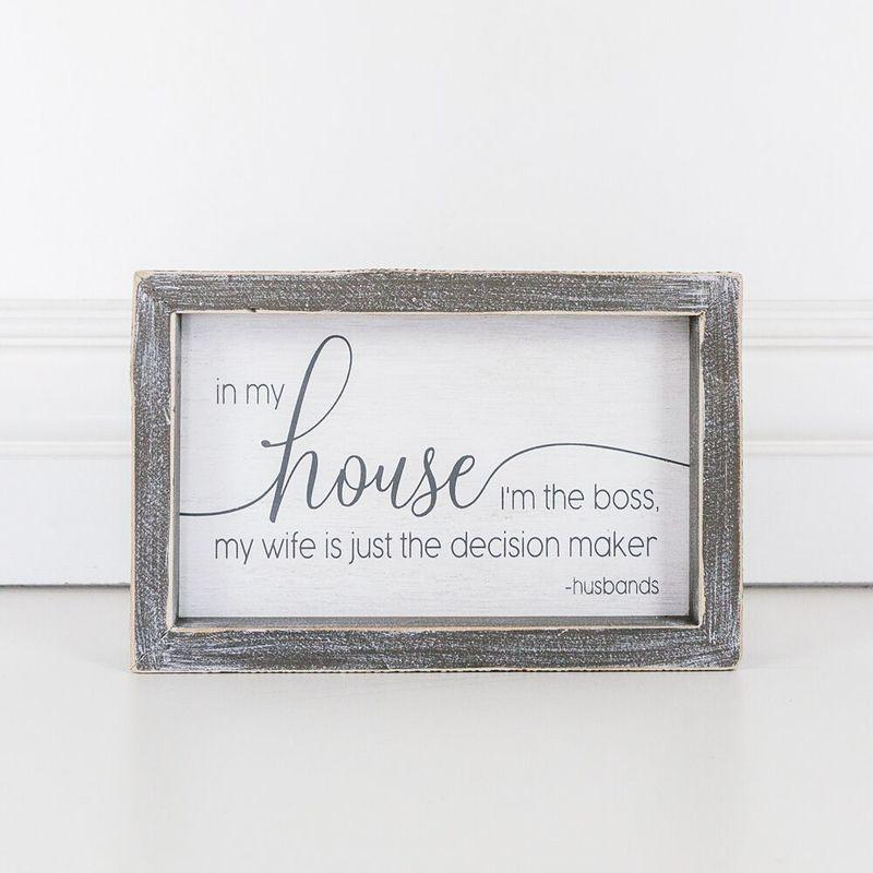 A humorous wooden sign that reads 'In My House I'm The Boss, My Wife Is Just The Decision Maker - Husbands', framed in white and grey.