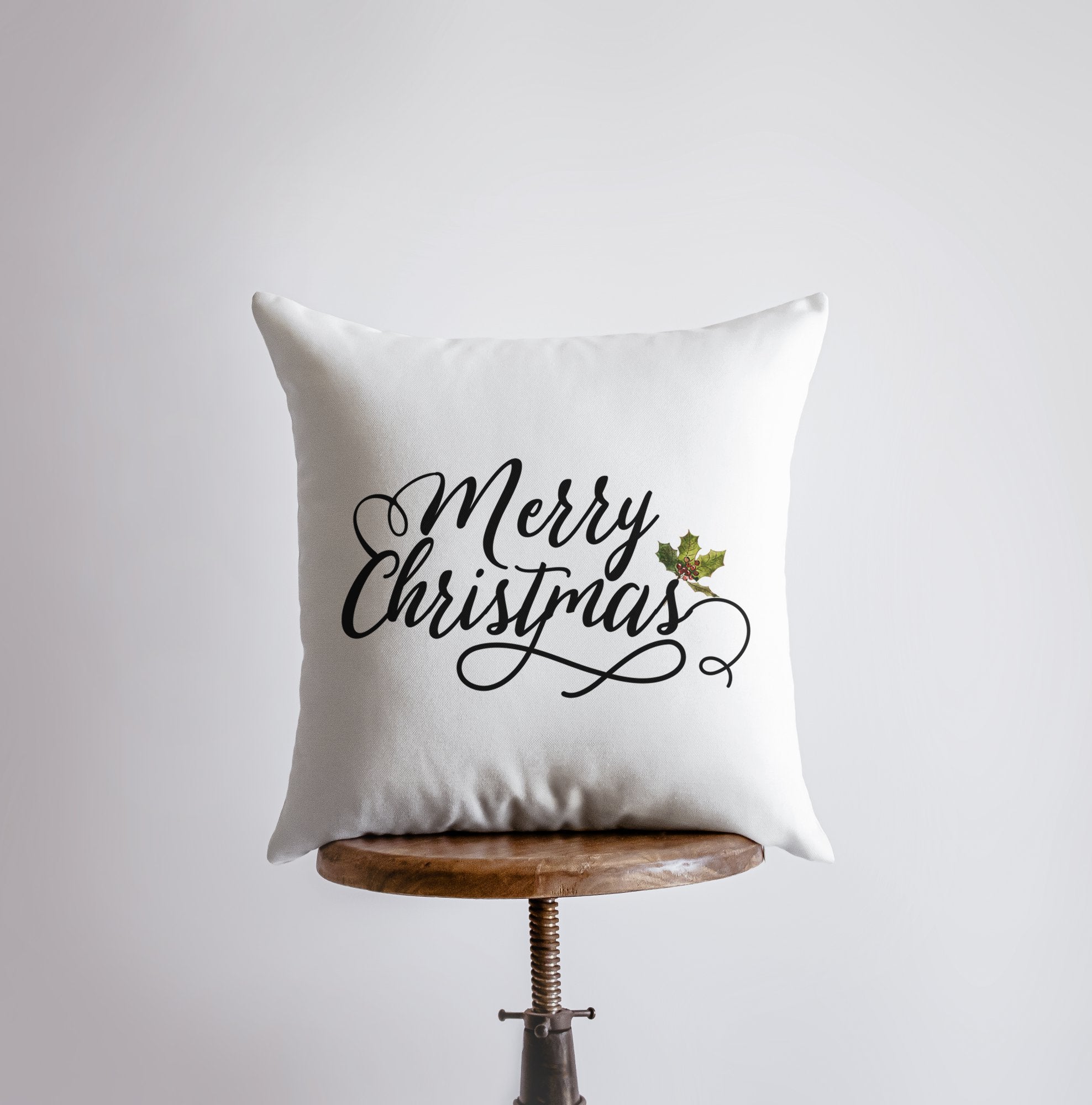 Merry Christmas throw pillow featuring black cursive lettering on a white background with a holly twig accent, perfect for holiday decor.