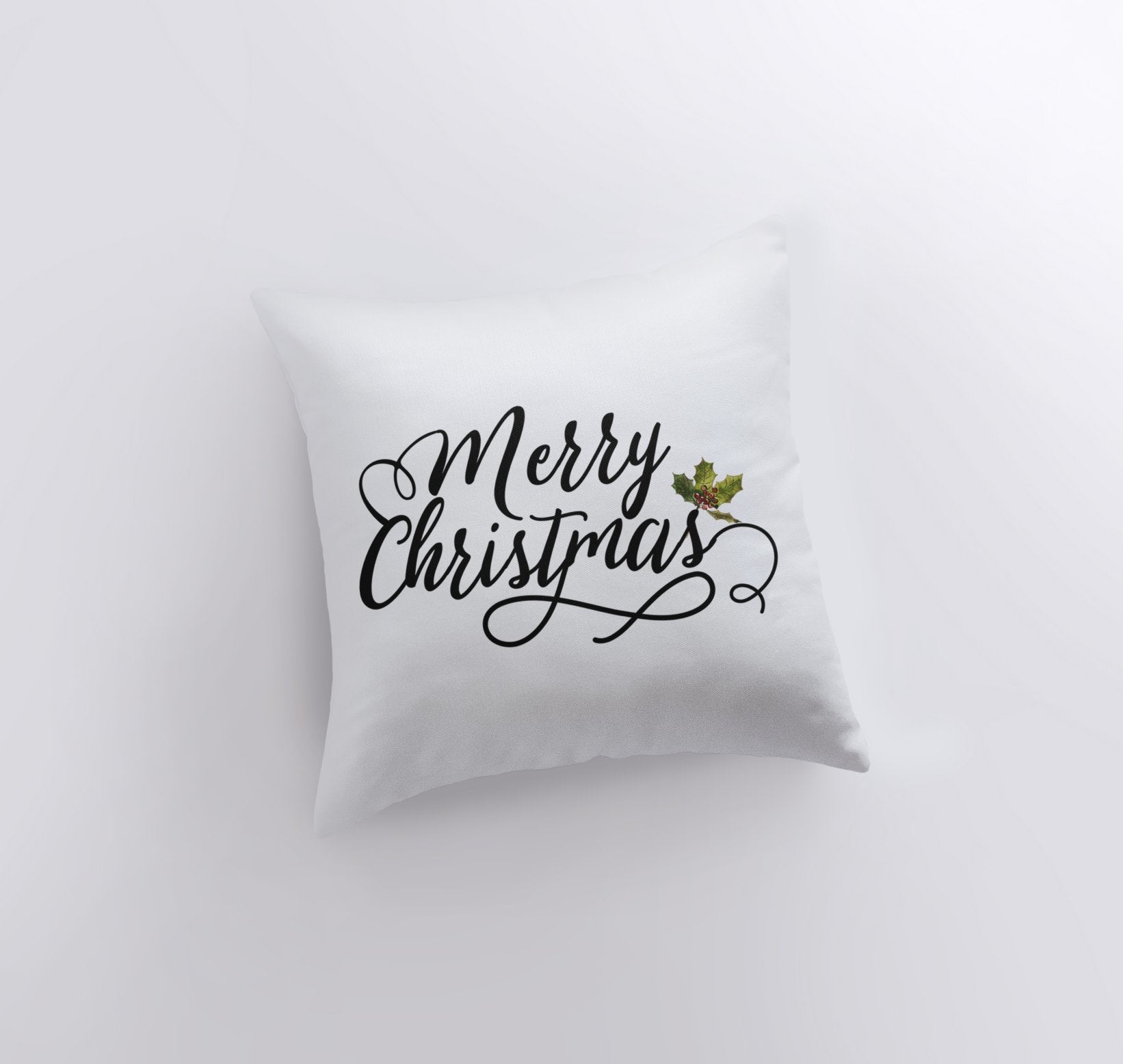 Merry Christmas throw pillow featuring black cursive lettering on a white background with a holly twig accent, perfect for holiday decor.