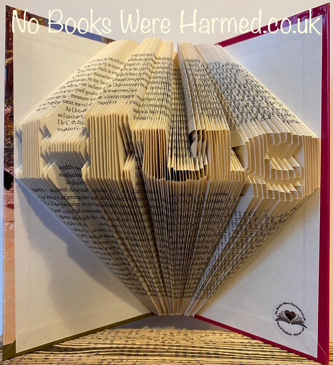 A handcrafted mini 'Hug' art piece made from folded pages of vintage books, showcasing intricate designs and unique colors.