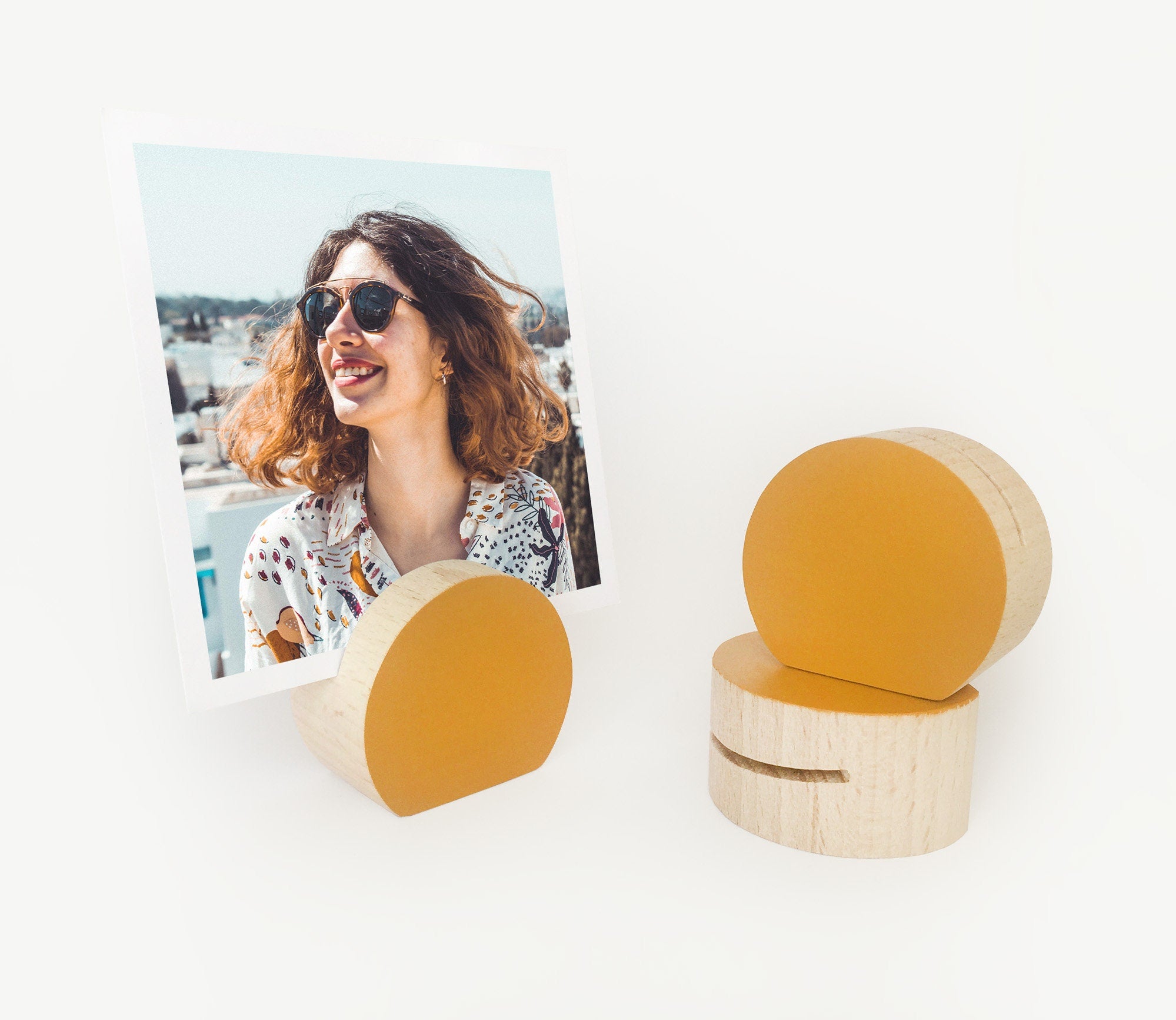 A handcrafted mustard moon shaped card holder made from eco-friendly wood, displaying small art prints and photos.