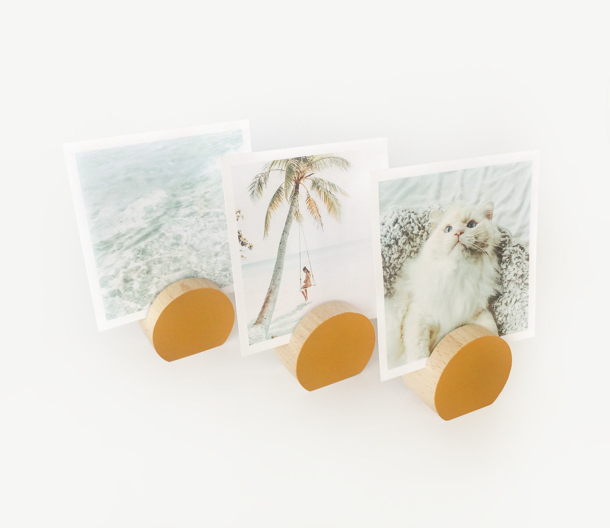 A handcrafted mustard moon shaped card holder made from eco-friendly wood, displaying small art prints and photos.