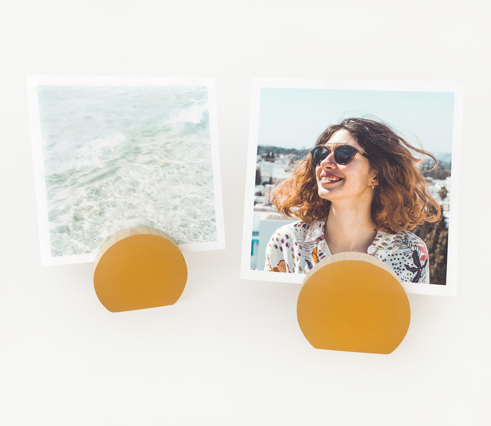 A handcrafted mustard moon shaped card holder made from eco-friendly wood, displaying small art prints and photos.