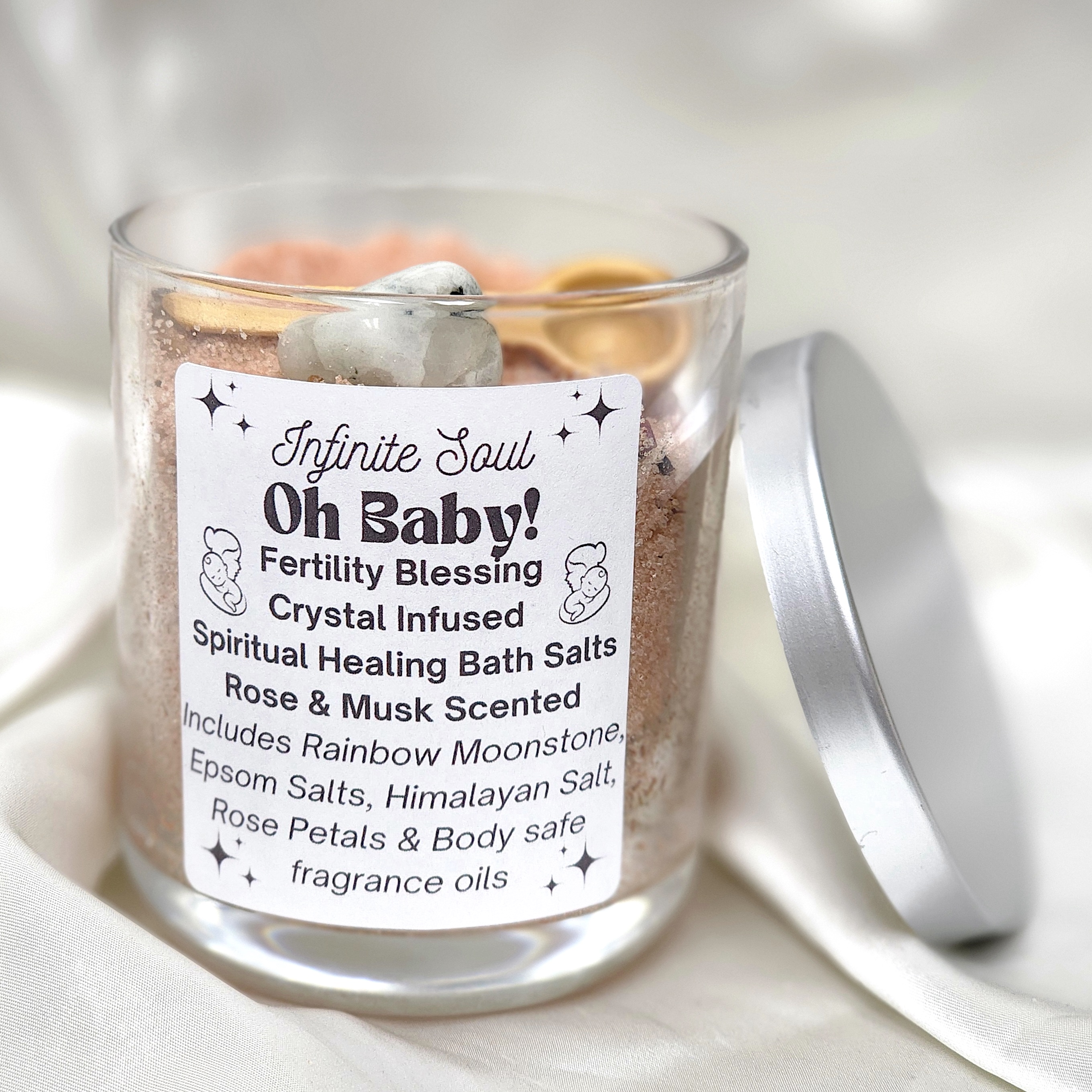 Oh Baby! Fertility Blessing Crystal Infused Bath Salts in a decorative jar with rose petals and a wooden spoon, featuring a chunk of Rainbow Moonstone.