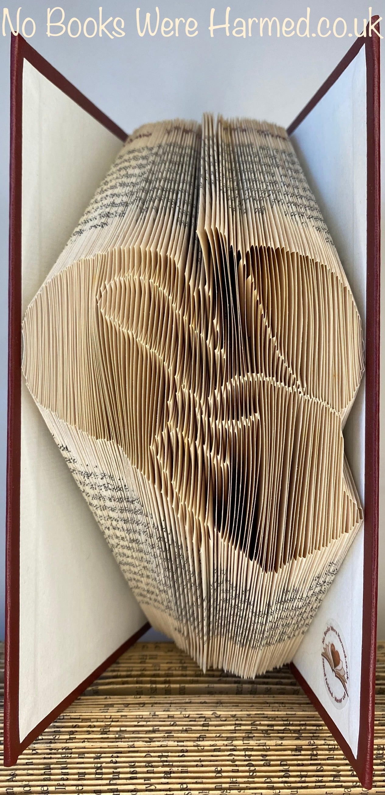 Art piece featuring a hand in a heart shape, crafted from the pages of vintage books, showcasing intricate hand folding techniques.