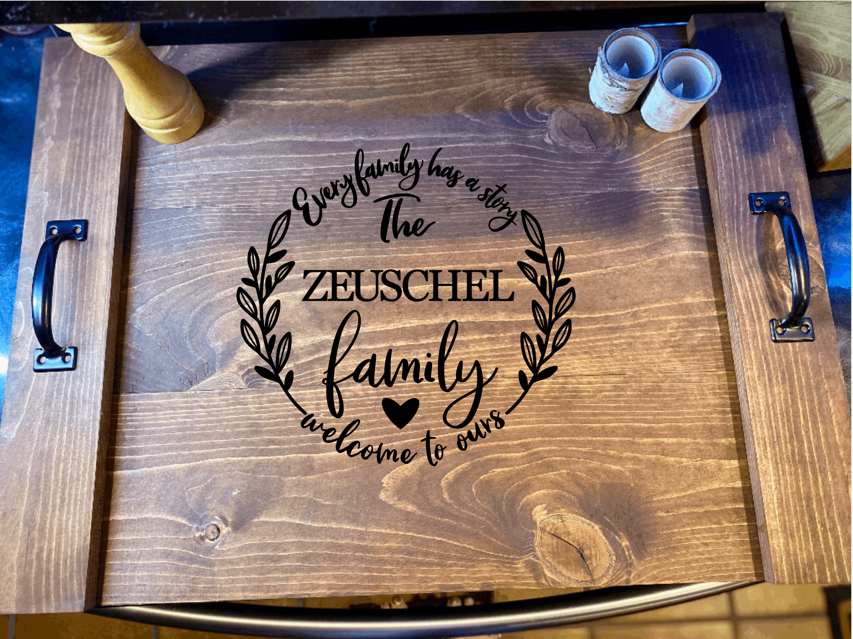 Personalized family name noodle board made of solid pine wood, stained in dark chestnut color, featuring black metal handles.