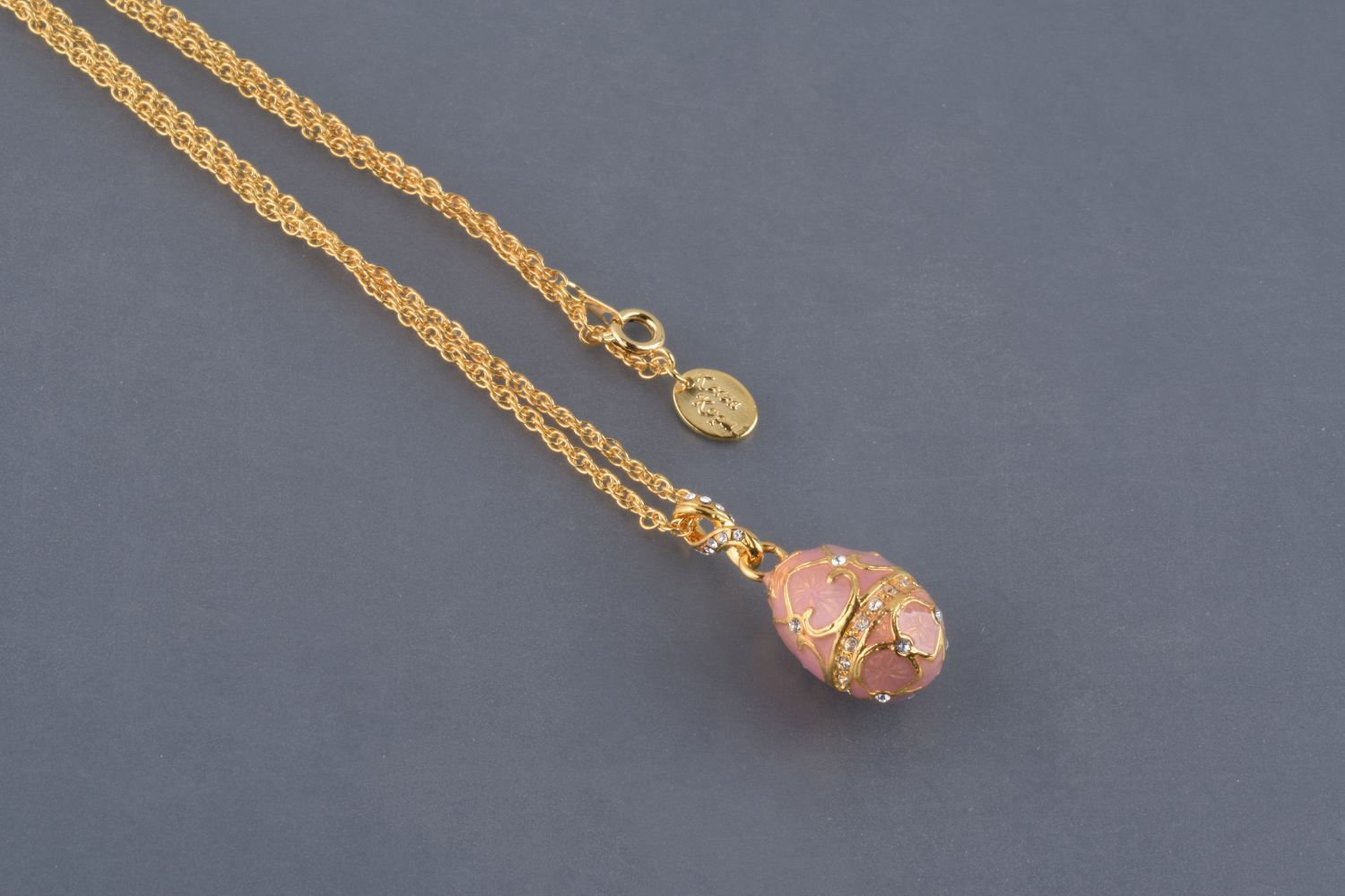 A beautiful pink egg pendant necklace adorned with Austrian crystals, showcasing intricate hand-painted enamel details and 24K gold plating.