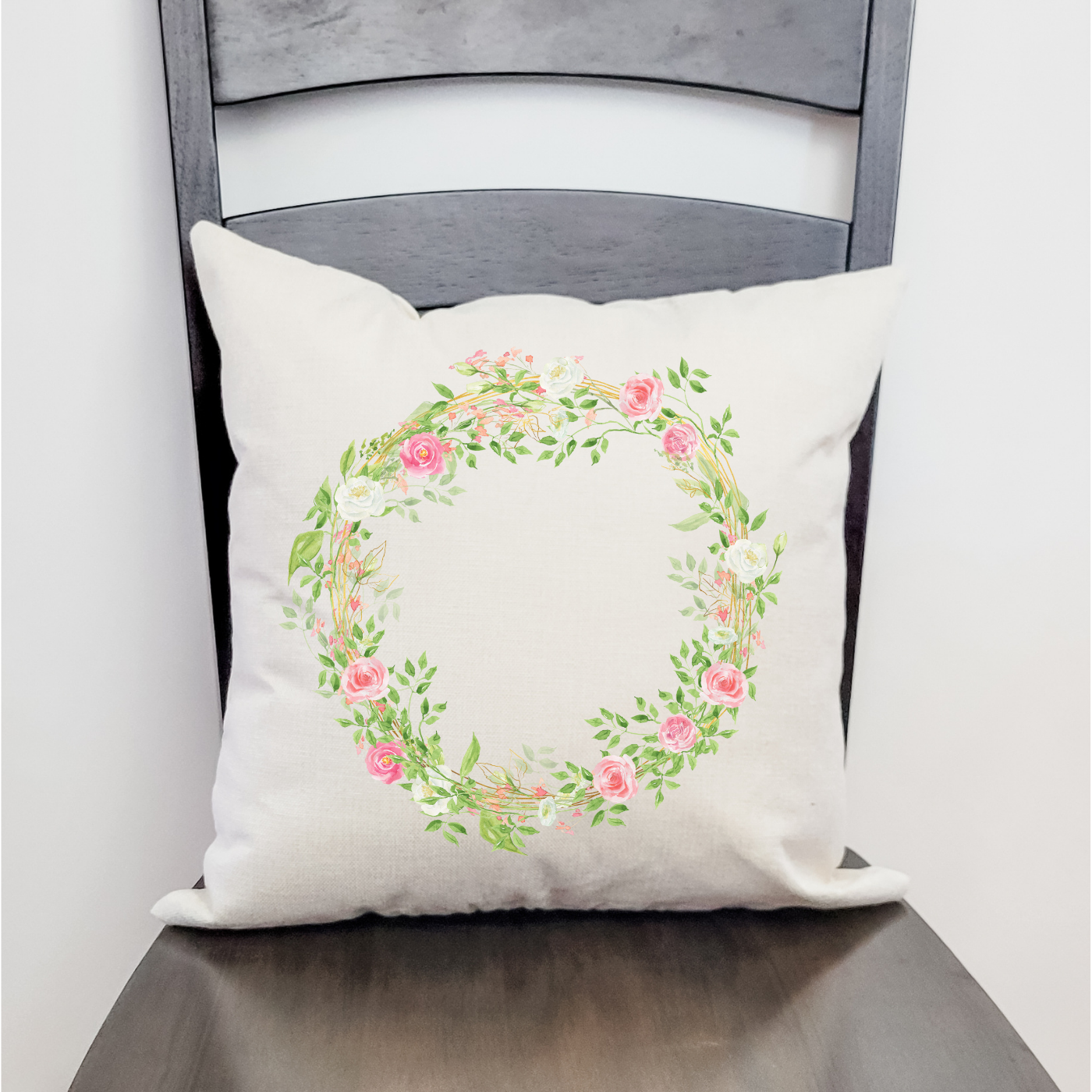 A soft pink wreath pillow cover featuring floral designs, perfect for spring decor, with a hidden zipper and available in beige or satin white.