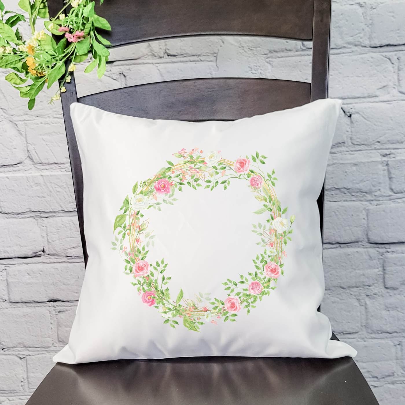 A soft pink wreath pillow cover featuring floral designs, perfect for spring decor, with a hidden zipper and available in beige or satin white.