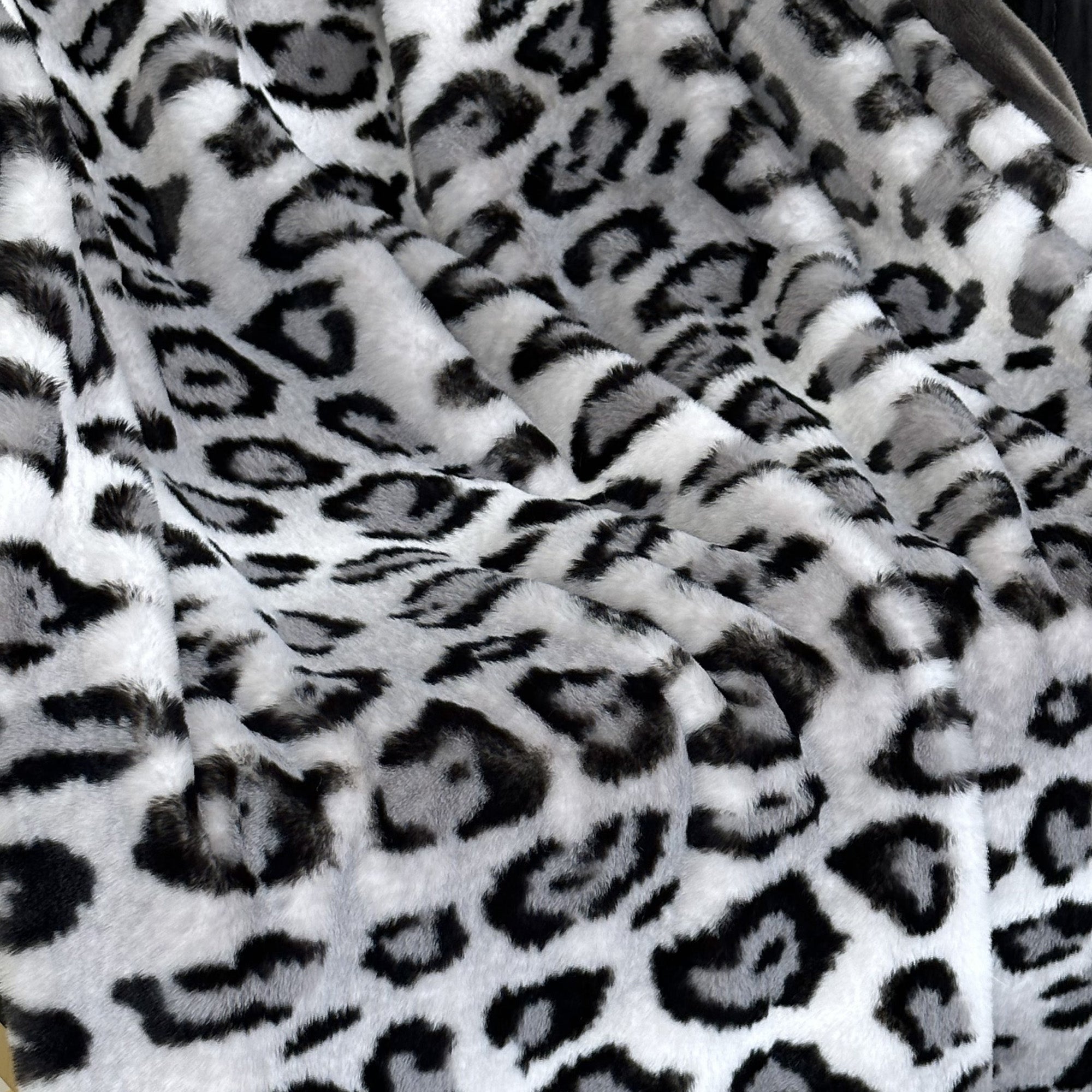 Plutus Gray Silver Jaguar Faux Fur Luxury Throw Blanket draped elegantly over a couch, showcasing its plush texture and stylish design.