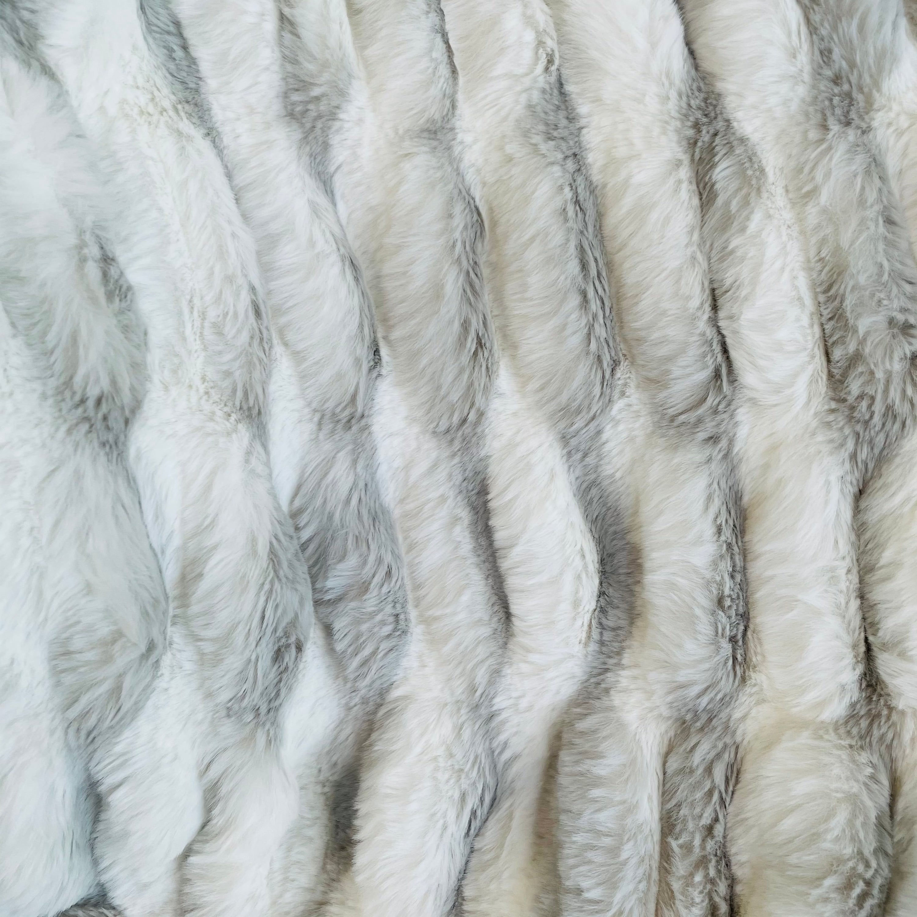 Plutus White Silver Snow Chinchilla Faux Fur Luxury Throw Blanket draped elegantly on a sofa, showcasing its plush texture and reversible design.