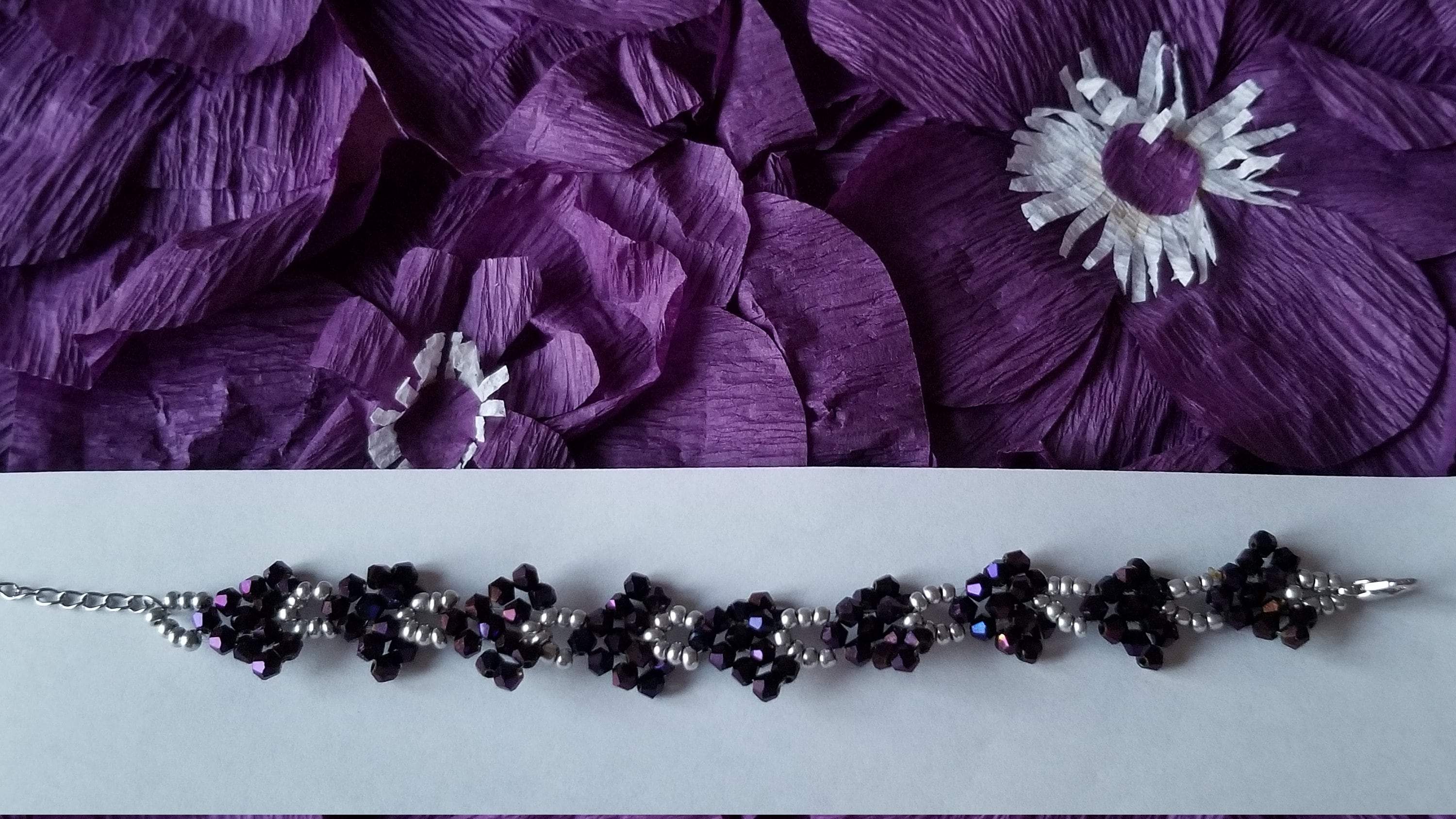 A stylish purple beaded bracelet featuring sparkly purple and silver beads arranged in a heart-shaped pattern on a stainless steel chain.